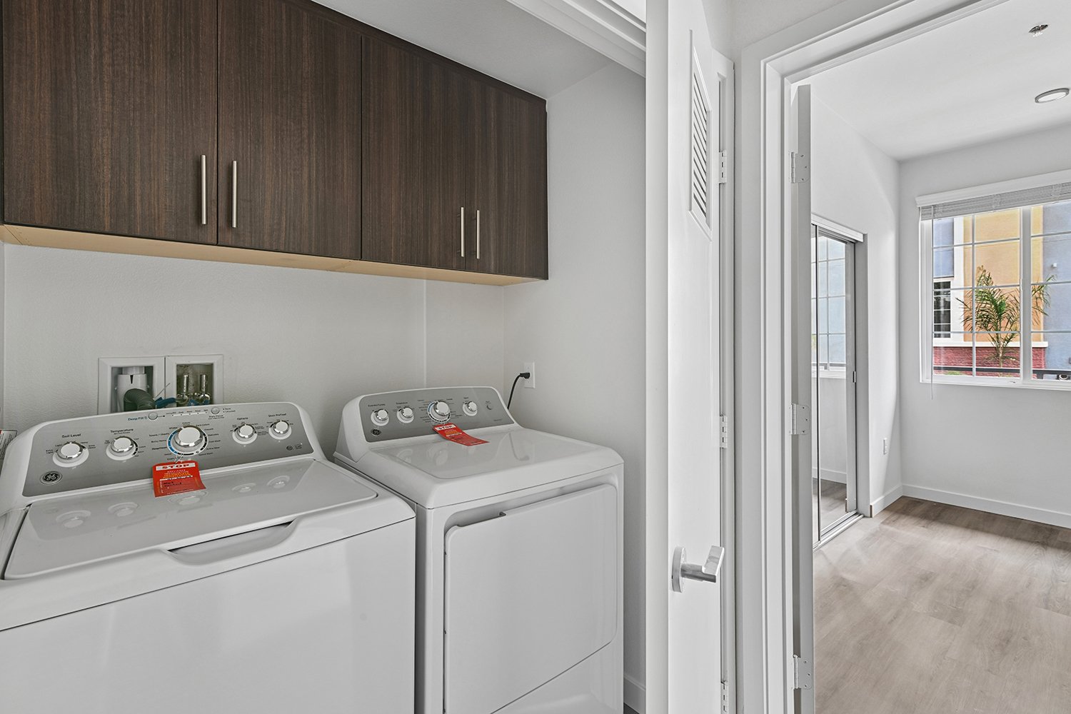 Full-sized washer and dryer in Rendezvous Phase II apartment home with overhead cabinetry for storage. 
