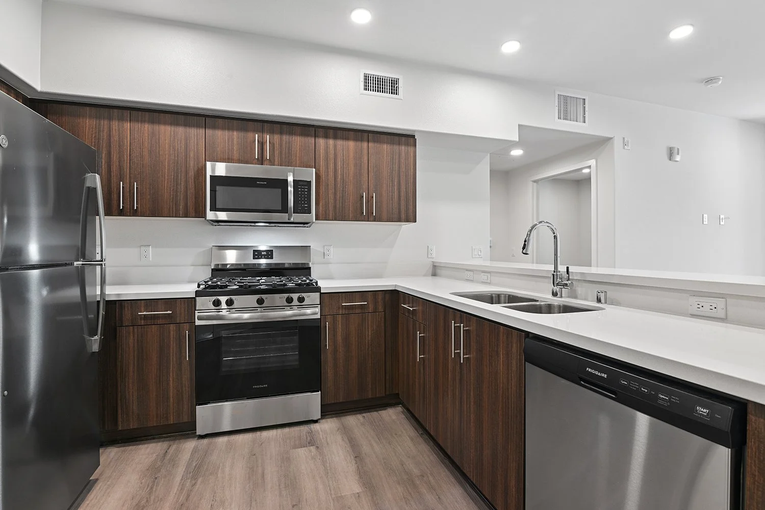 Kitchen in Rendezvous Phase II apartment home with plank flooring, stainless appliances, quartz countertops, and a large breakfast bar overlooking the living area and doors leading to private patio. 