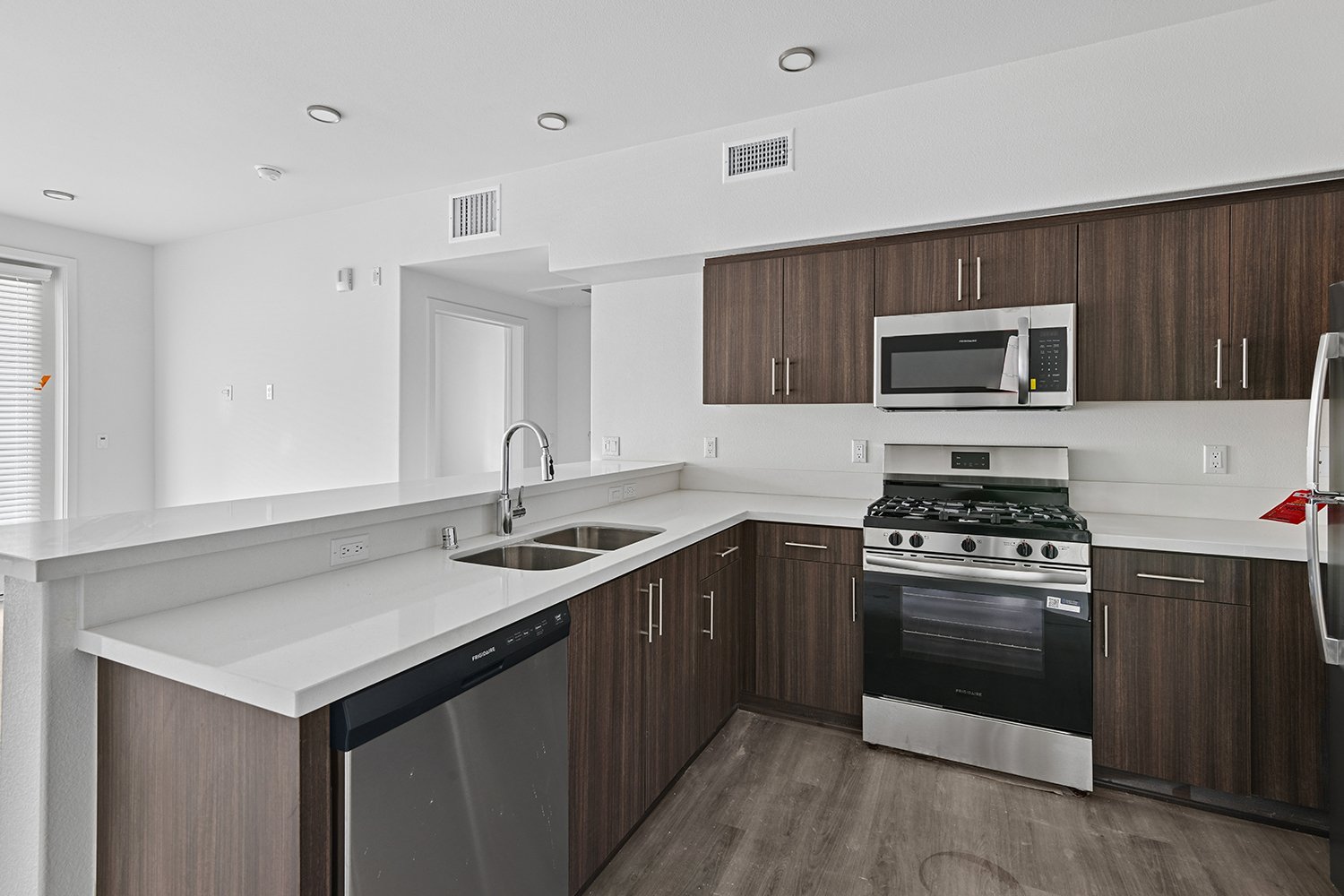 Kitchen in Rendezvous Phase II apartment home with wood-style plank flooring, quartz countertops, stainless steel appliances and modern dark walnut cabinetry. 