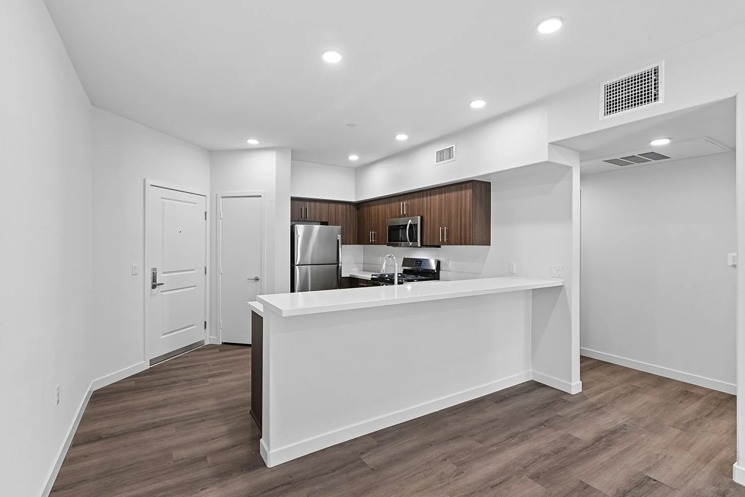 Kitchen in Rendezvous Phase II apartment home with plank flooring, stainless appliances, quartz countertops, and a large breakfast bar overlooking the living area and doors leading to private patio. 