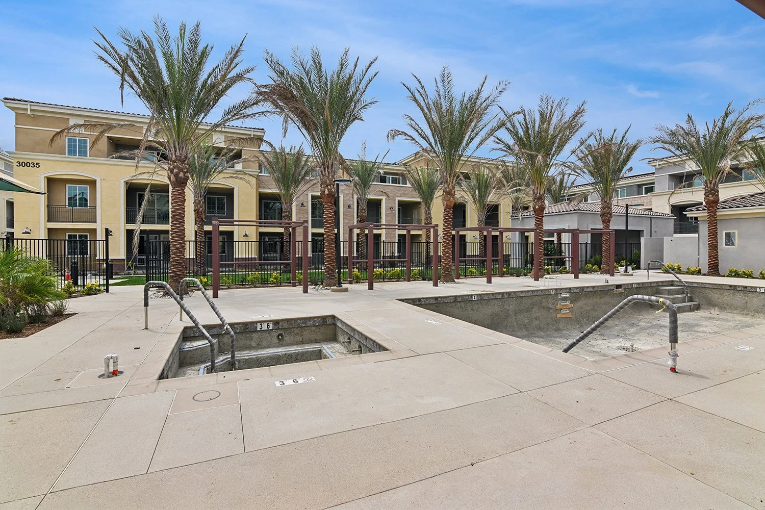 Resort-style pool area at Rendezvous Phase II apartments with a relaxing spa and sparkling pool, cabanas, and palm trees lining the fence for ultimate relaxation and luxury. 
