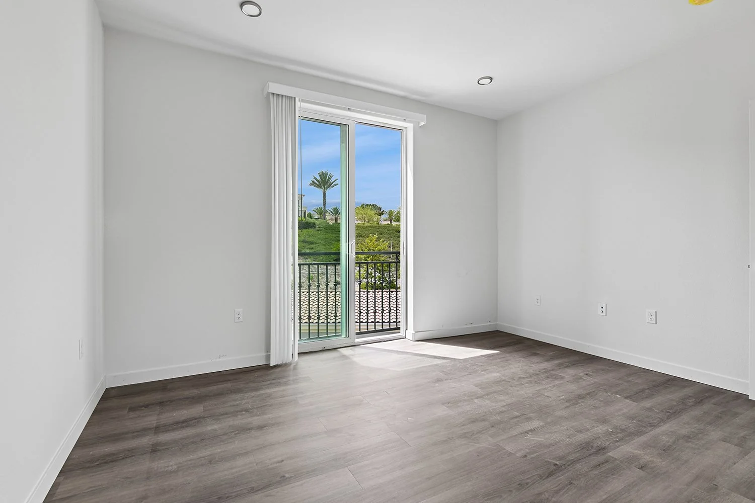 Gorgeous bedroom in Rendezvous Phase II apartments with wood-style plank flooring, and floor to ceiling window with decorative Juliet balcony for charm and luxury. 