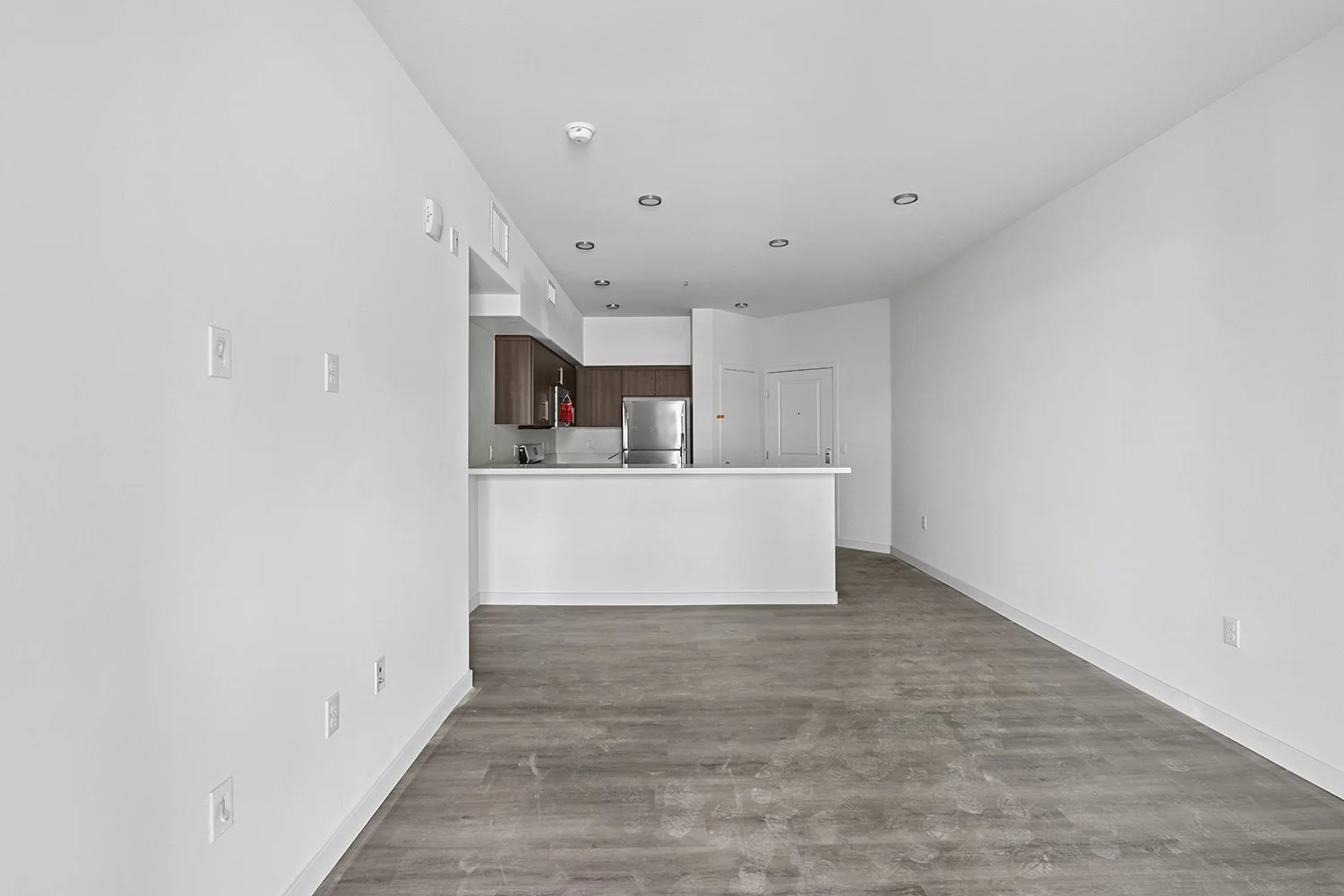 Living area leading into kitchen in Rendezvous Phase II apartment home with wood-style plank flooring and gorgeous kitchen with quartz countertops, stainless steel appliances and modern dark walnut cabinetry. 