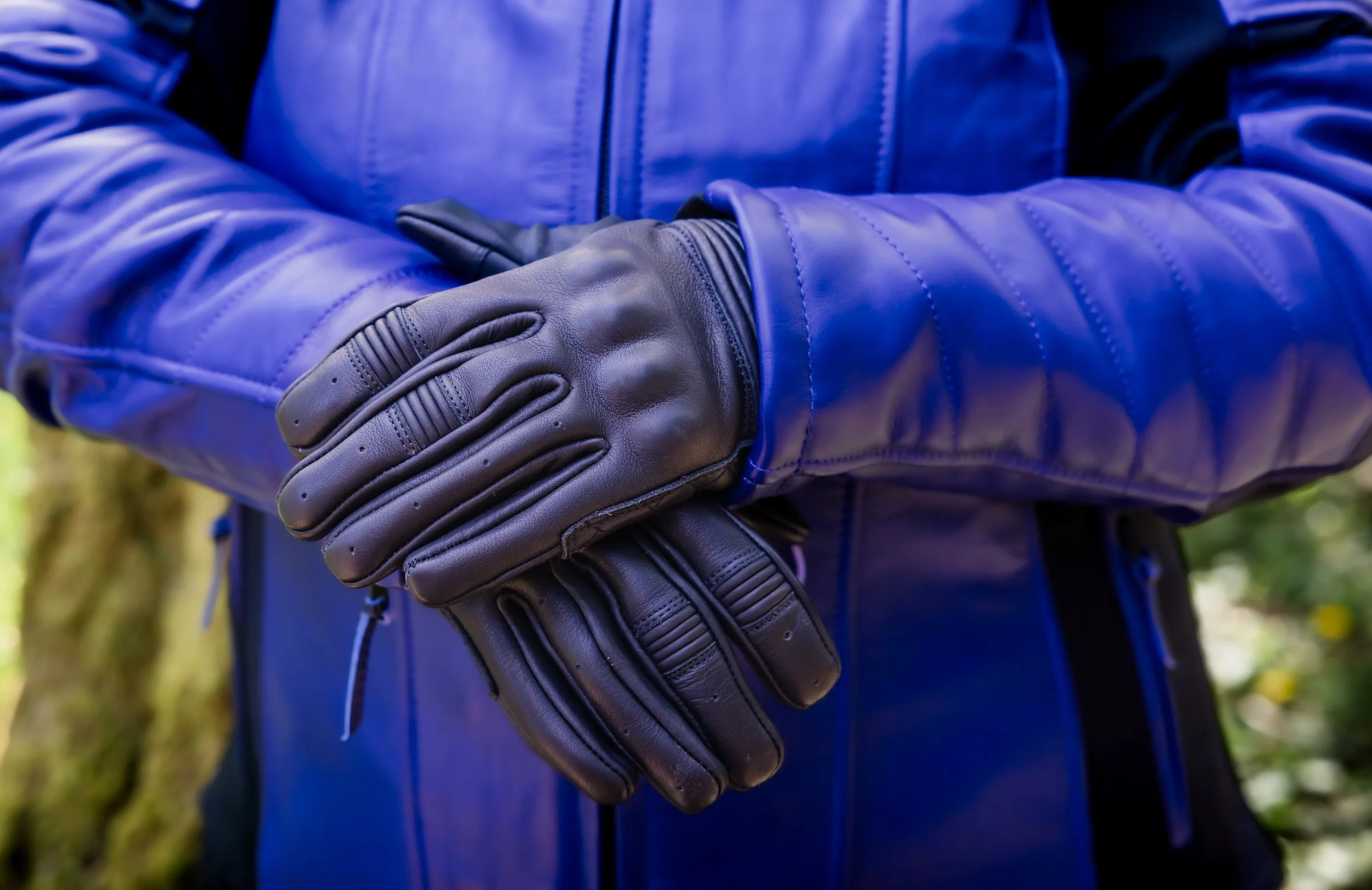 Person wearing black gloves and a blue jacket, holding a black leather backpack outdoors.