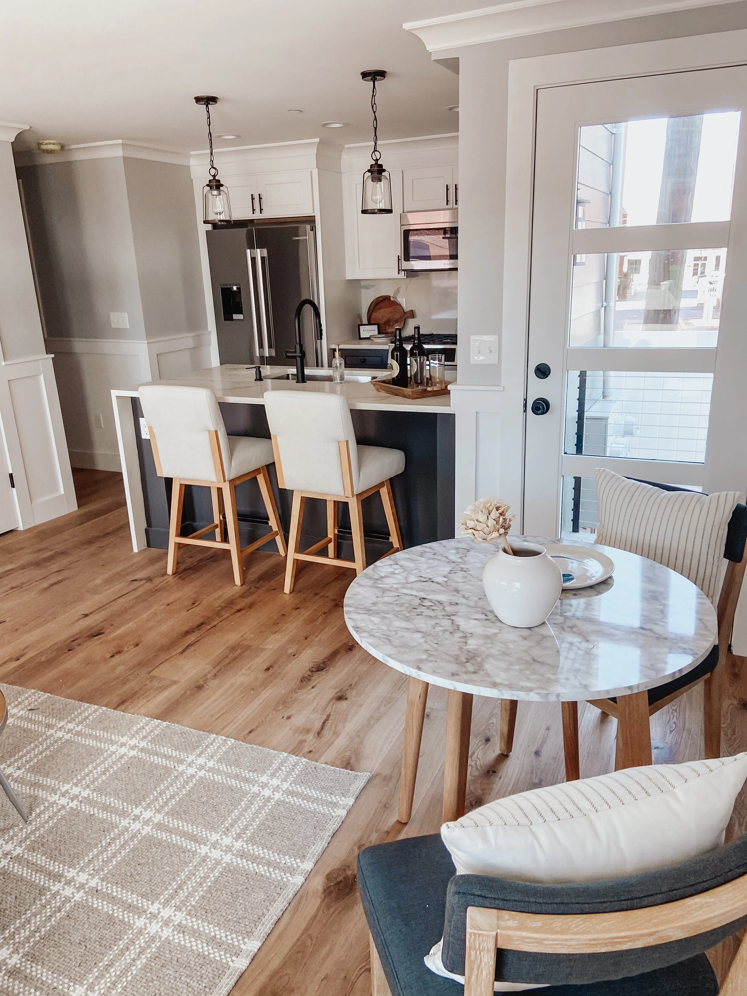 Modern kitchen and dining area with round marble table and chairs, kitchen island with counter, pendant lights, stainless steel appliances, and wooden flooring