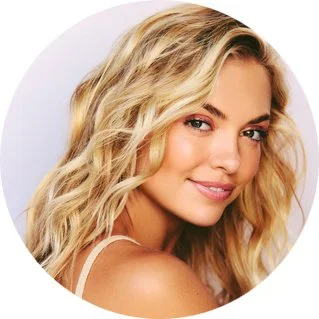 Close-up portrait of a smiling woman with blonde, wavy hair and light makeup.