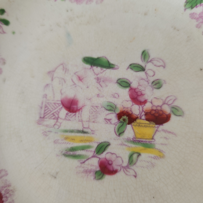 Close-up of an antique ceramic plate decorated with delicate pink and green floral motifs. Fine crazing covers the glaze, and the faded decoration shows the gentle effects of age and use.