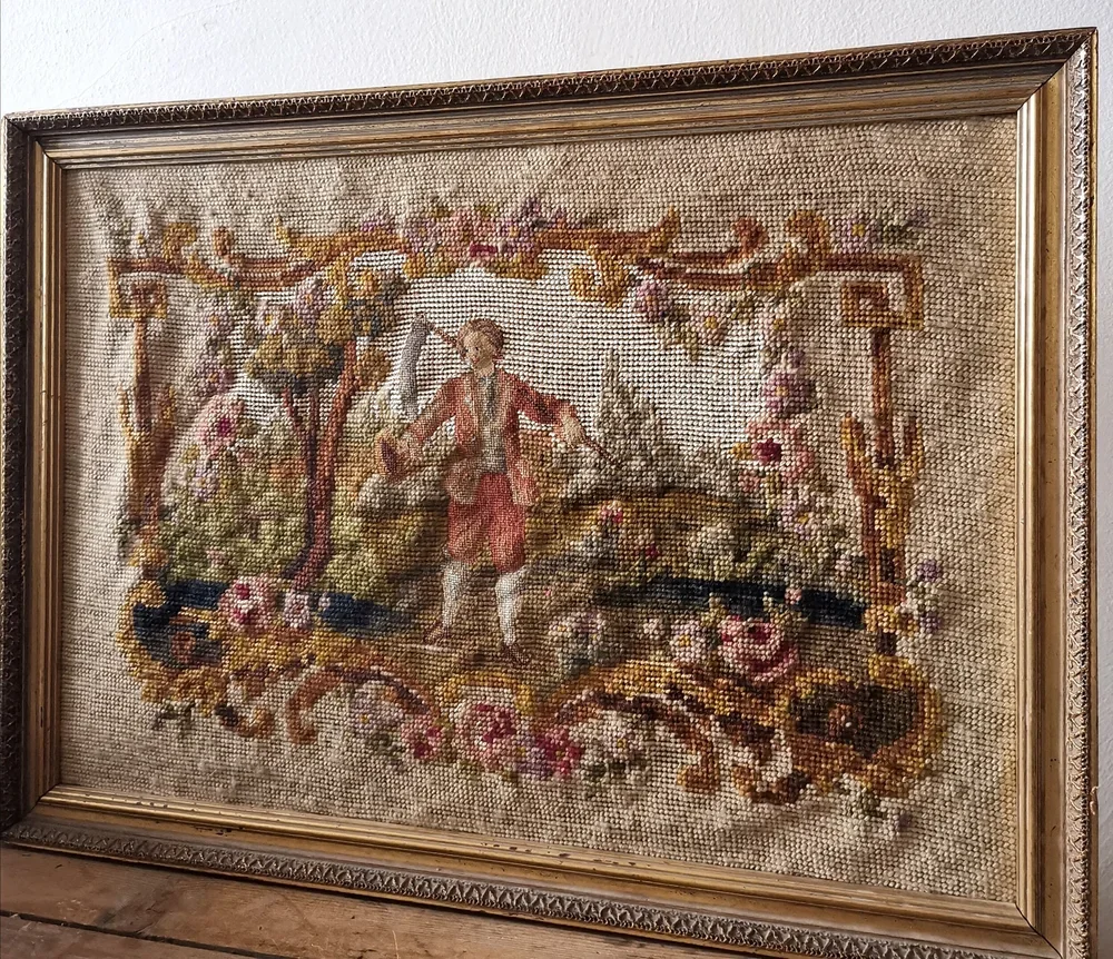Alt text: Framed antique French needlepoint showing a rustic harvest figure in a pastoral landscape