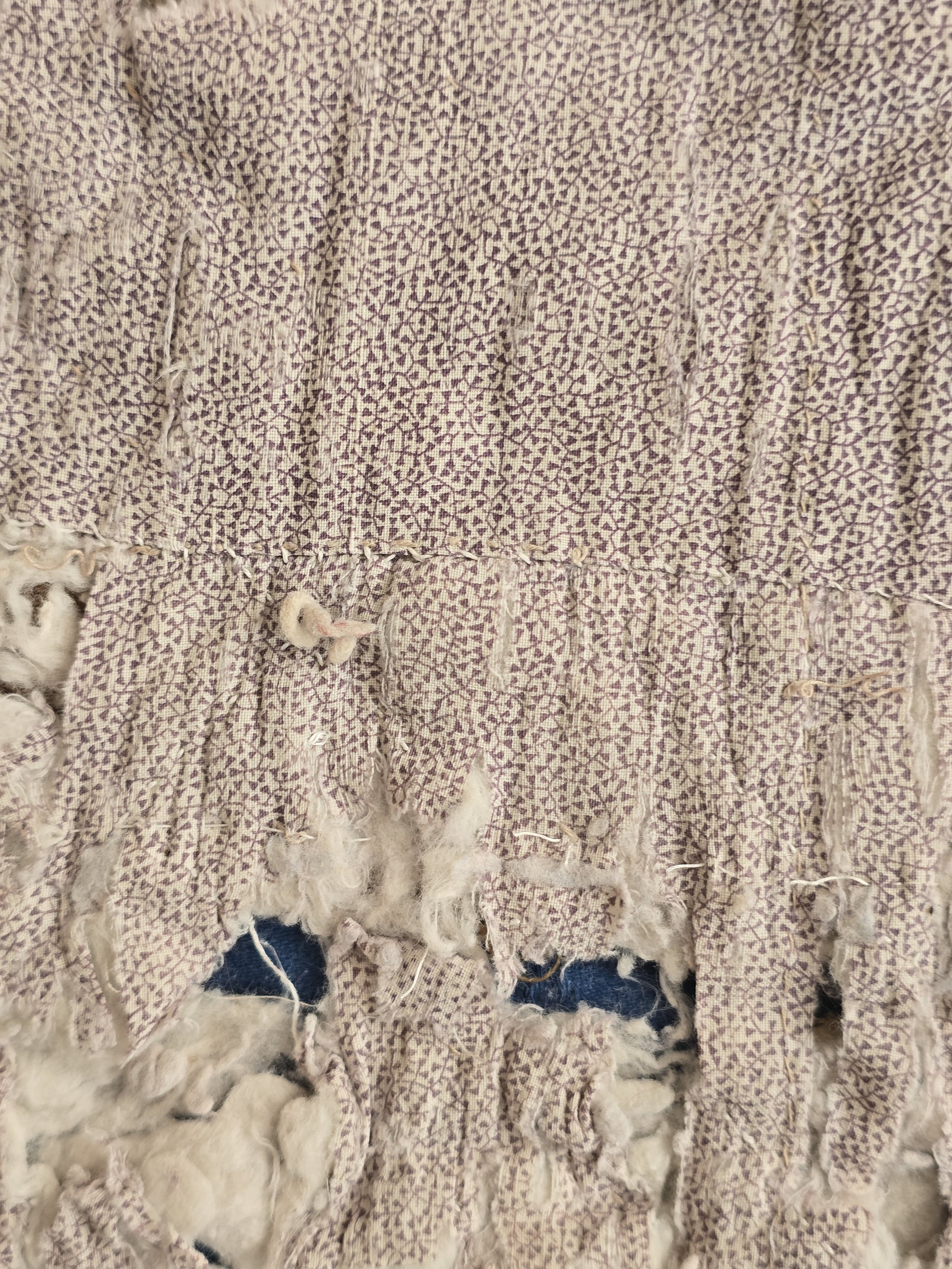 Worn French quilt fragment showing remnants of faded pink and green floral beneath the damaged surface.