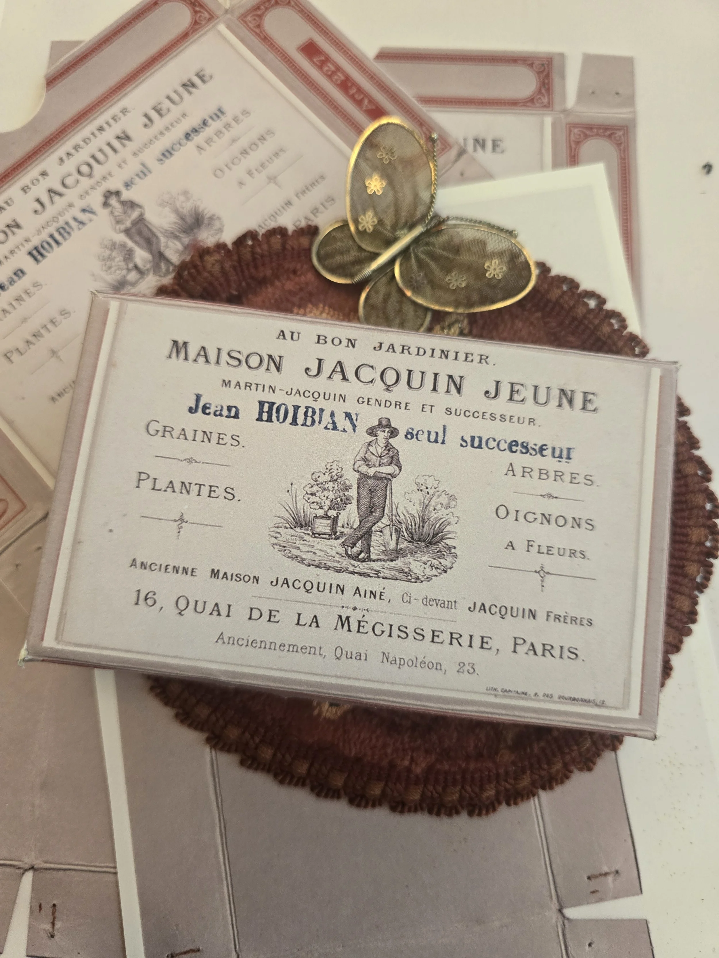Handmade French seed merchant box featuring antique Maison Jacquin Jeune Paris imagery, styled with vintage textiles and a butterfly ornament.