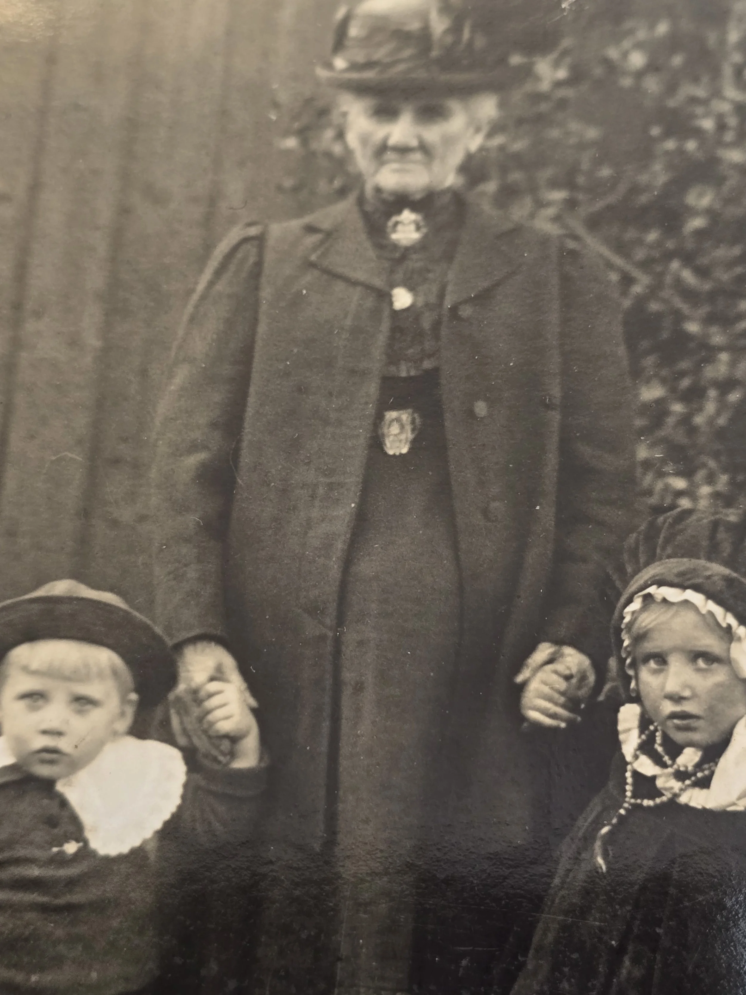 Detail of elderly woman in long dark dress and hat with two children in an early family photograph.