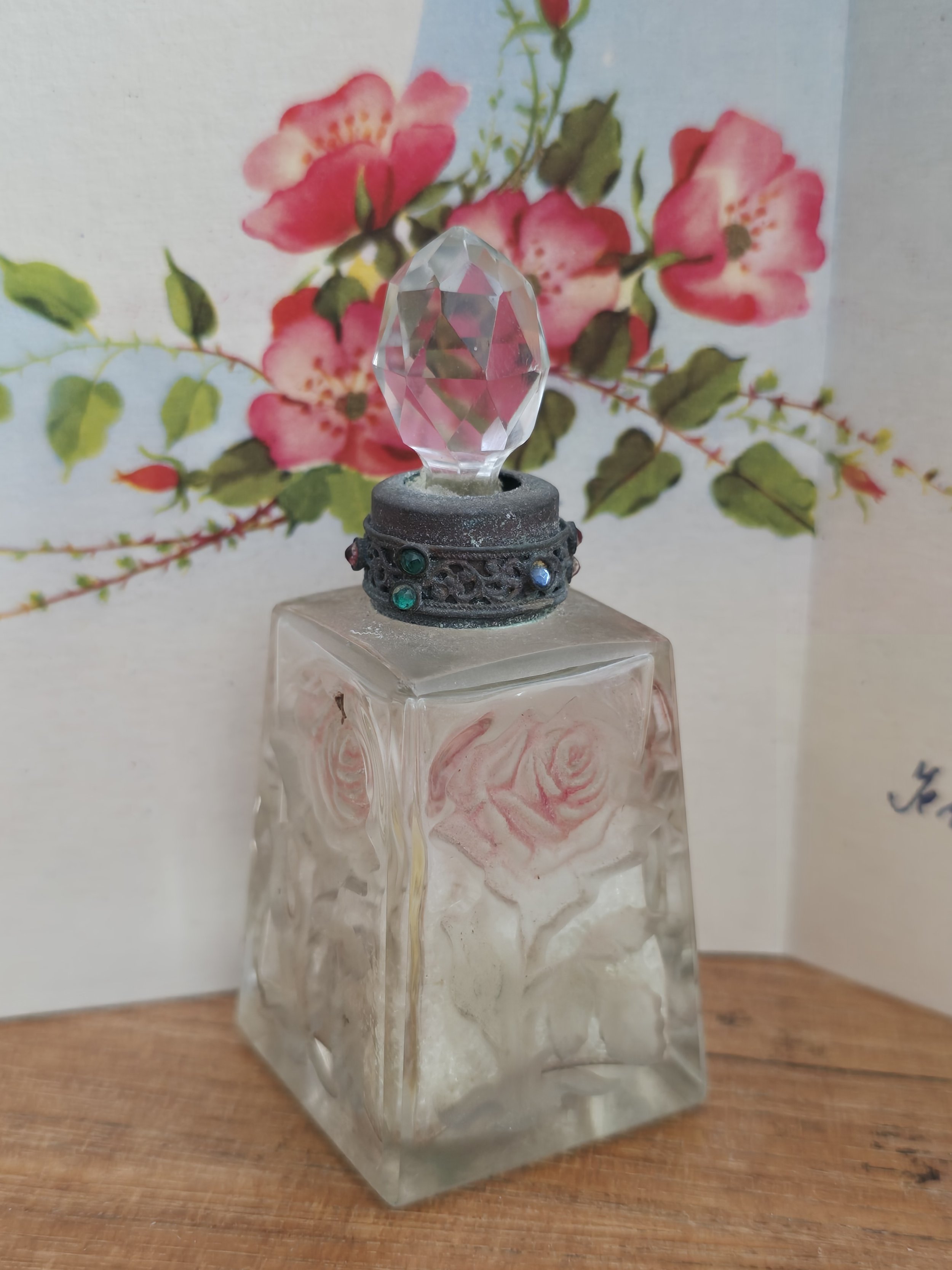 Antique frosted glass perfume bottle with moulded rose decoration and faceted crystal-style stopper.