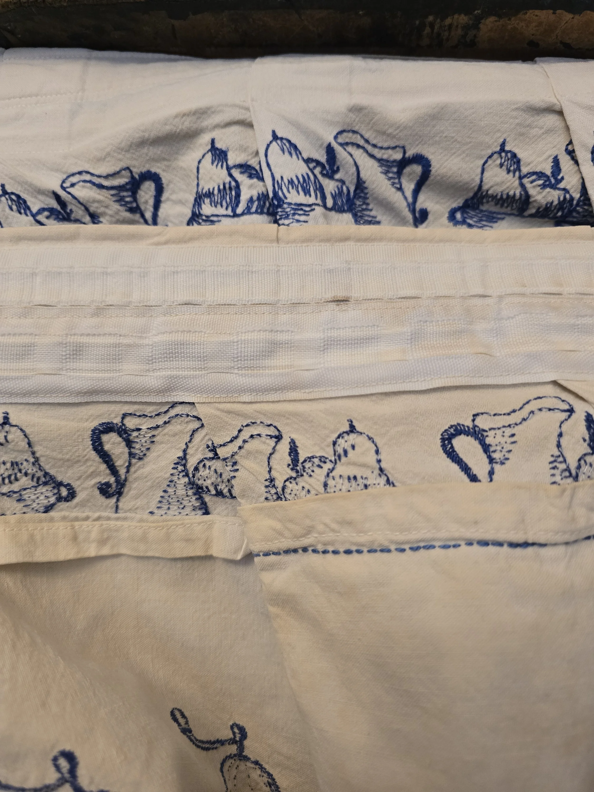 Reverse of vintage embroidered cotton valance showing original stitched heading, seams and blue kitchen-themed embroidery.