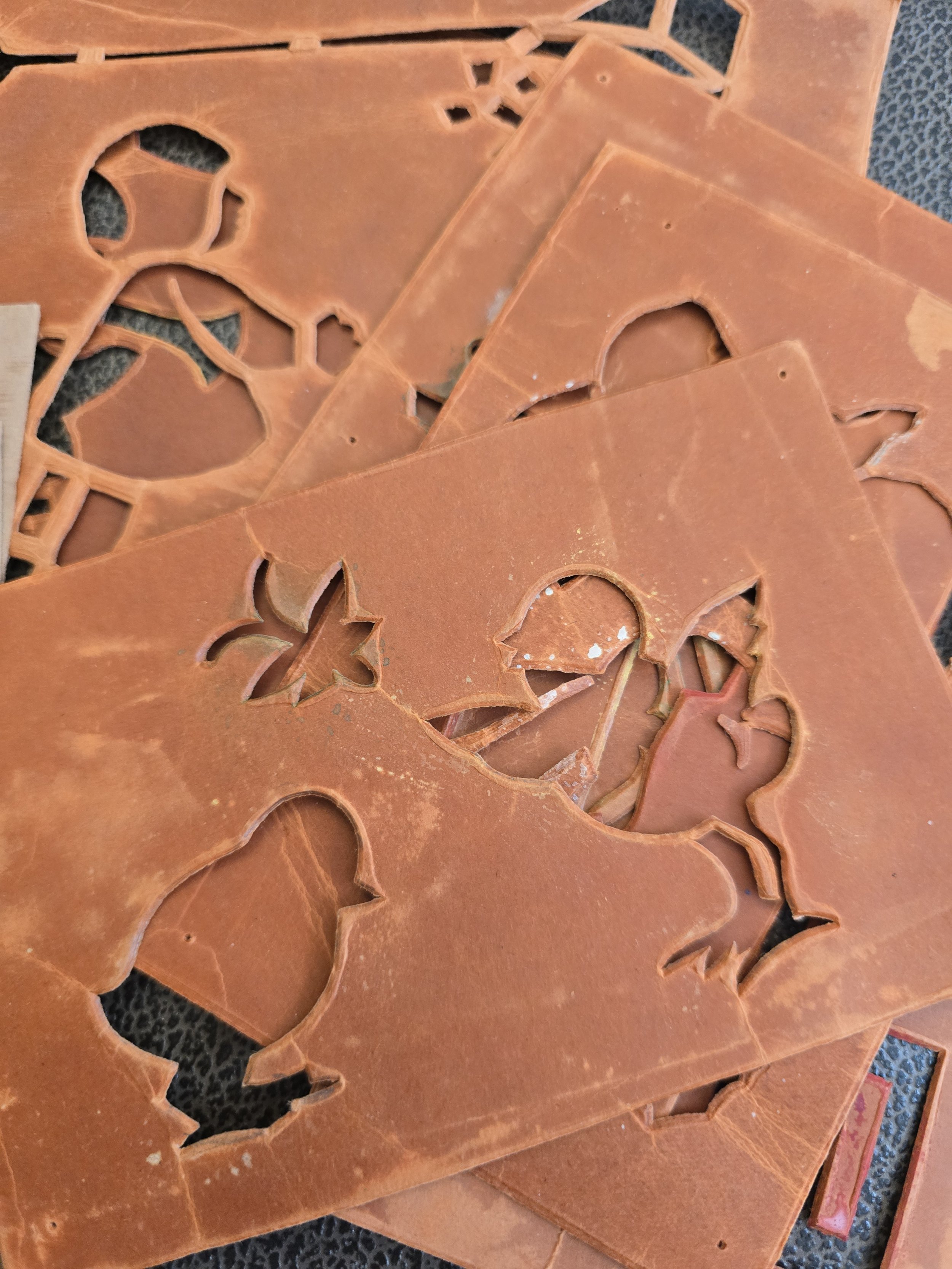 Large terracotta-red vintage card stencil with cut-out bird and floral motifs, showing a beautifully worn surface.
