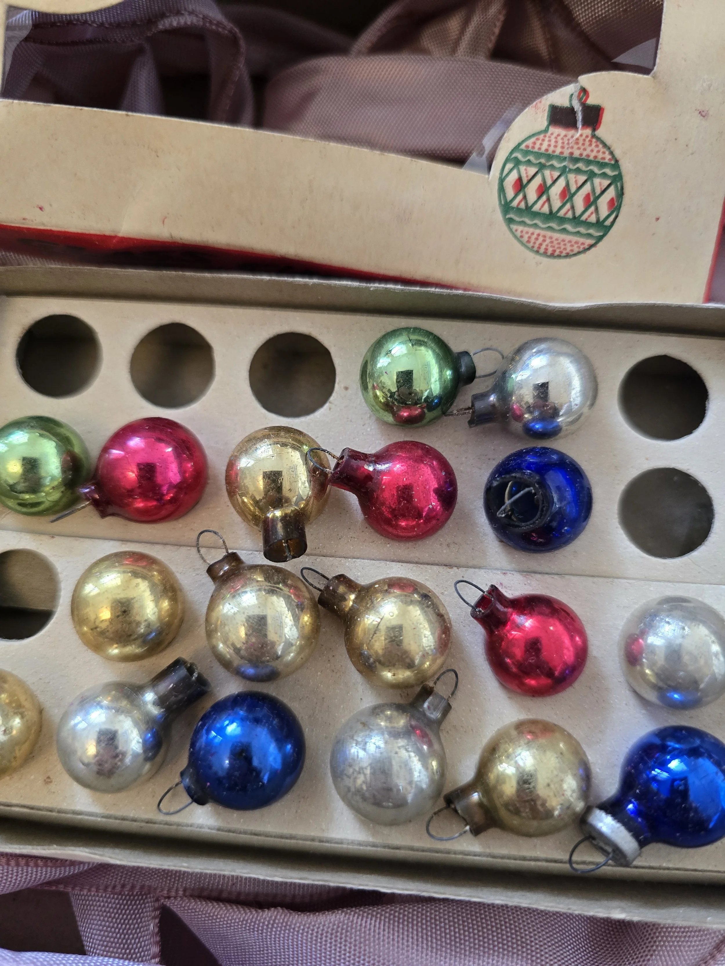 Eighteen miniature vintage Woolworth glass baubles arranged in their original cardboard tray, with six empty spaces.