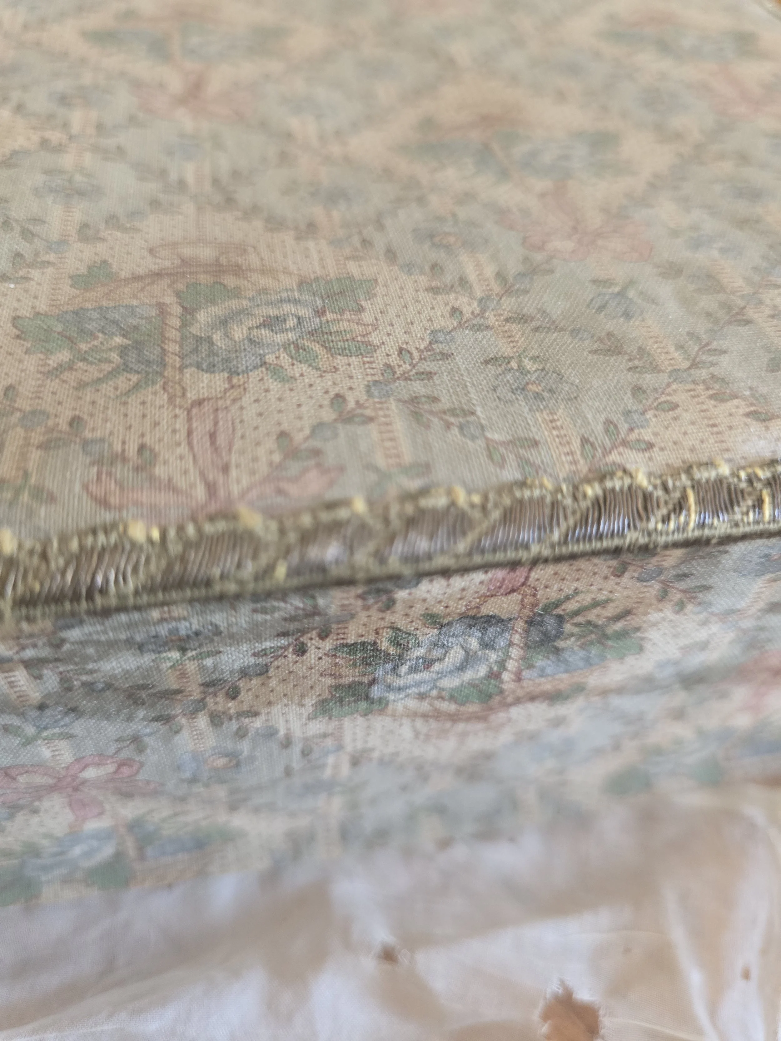 Detail of faded antique French fabric showing pink ribbon bow, blue flowers and trailing floral garlands.