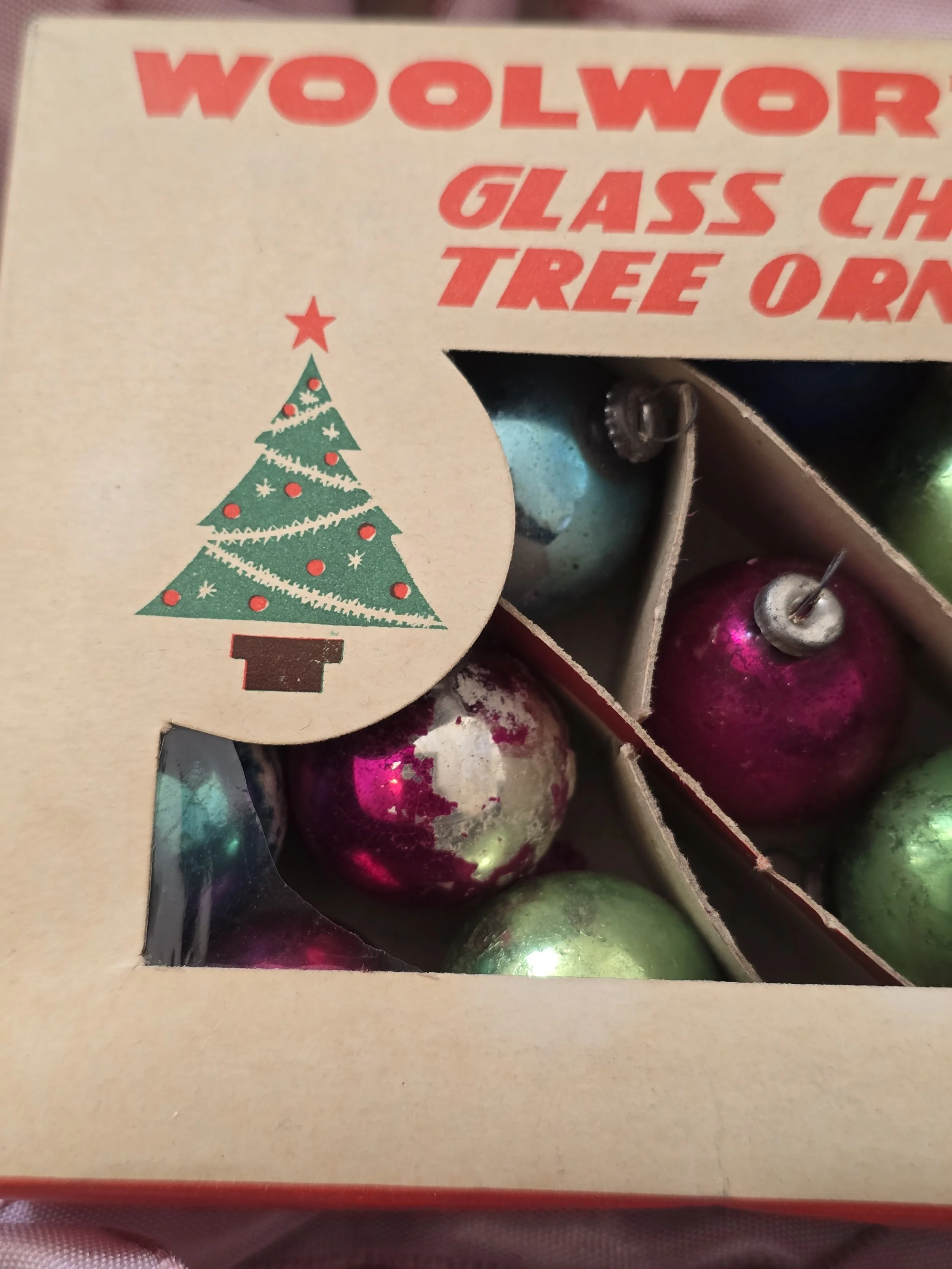 Close-up of the Woolworth Christmas ornament box showing worn cardboard dividers and vintage glass baubles with faded painted finishes.