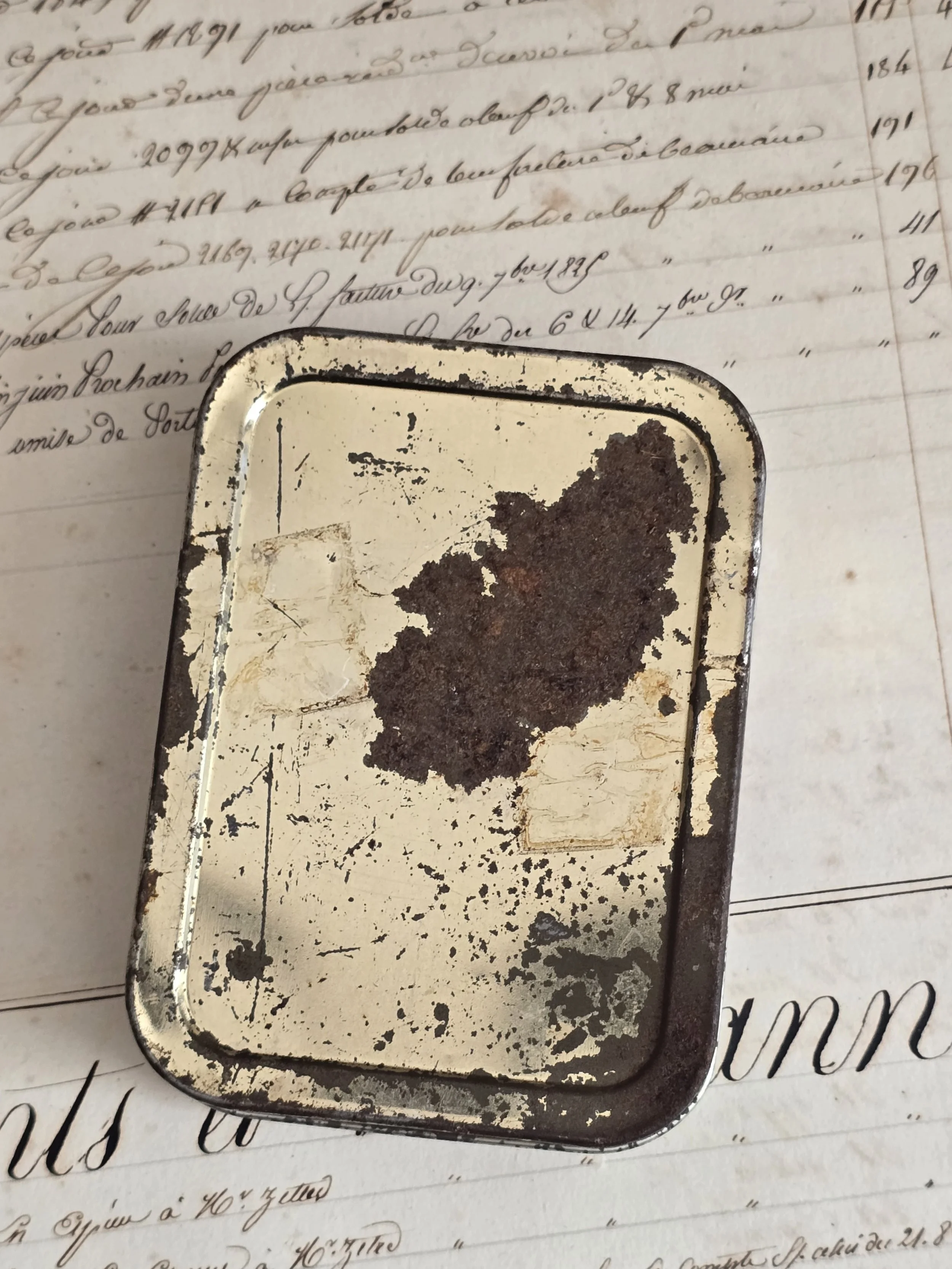 Reverse of vintage metal portrait tin showing original heavily worn cream finish, scratches, marks and areas of surface loss.