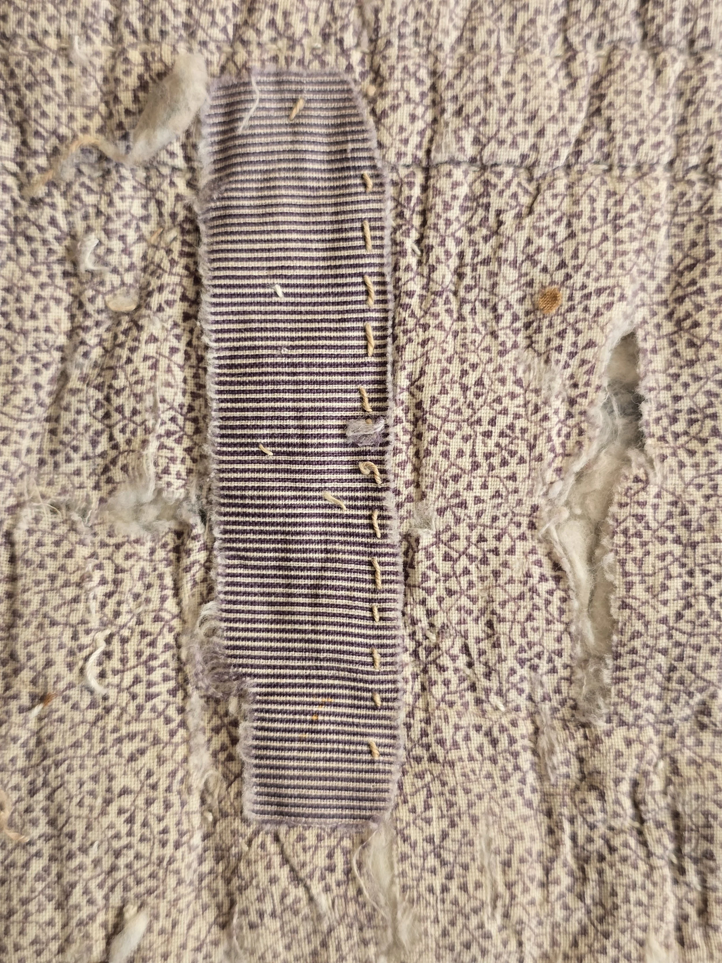 Antique French quilt fragment with faded purple printed cotton and exposed layers.