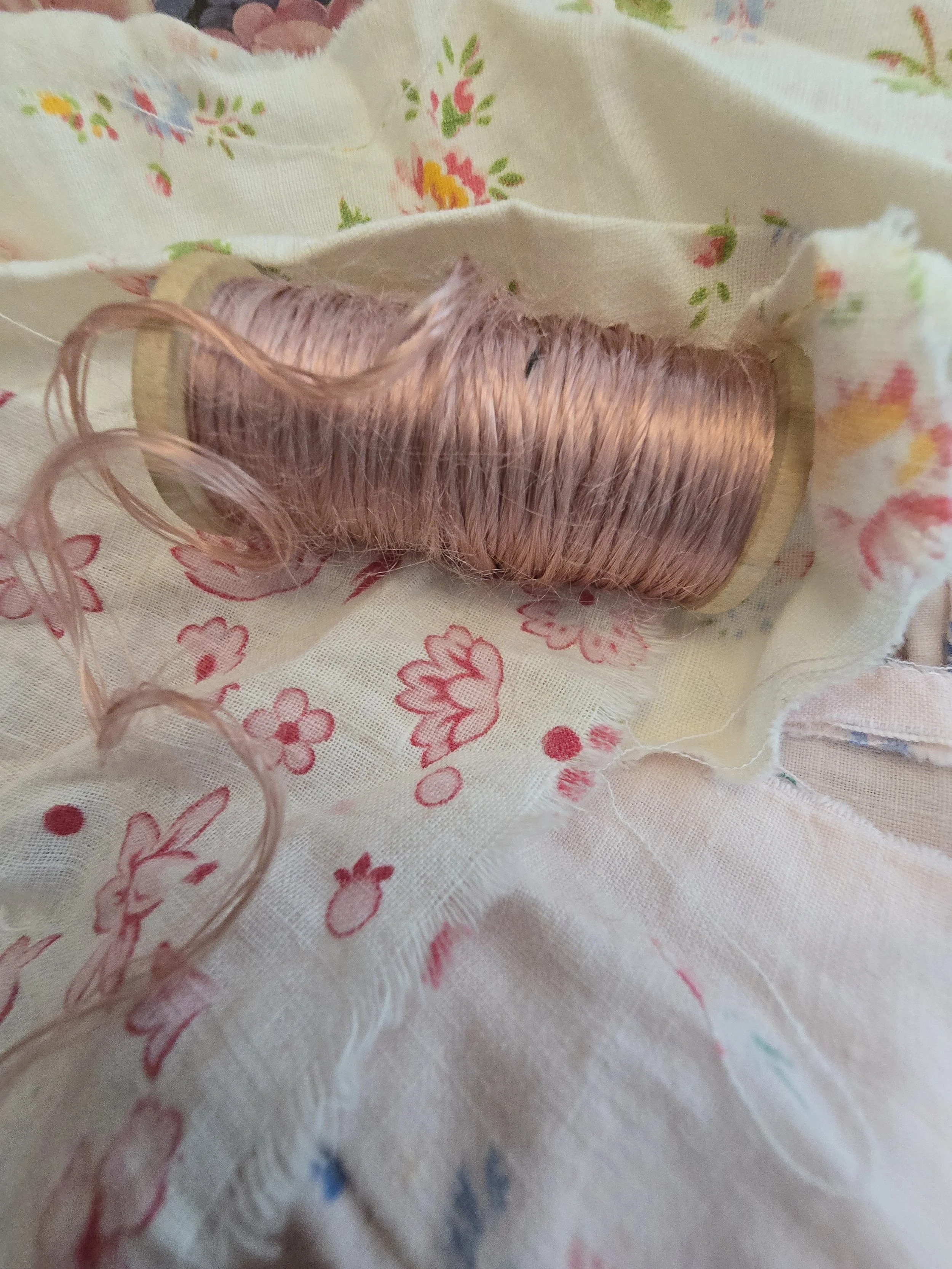 Soft pink vintage thread with silk-like sheen wrapped around a wooden haberdashery spool.