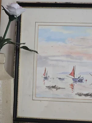 Framed Downderry Beach watercolour styled against wall with flower beside, coastal artwork in muted colours