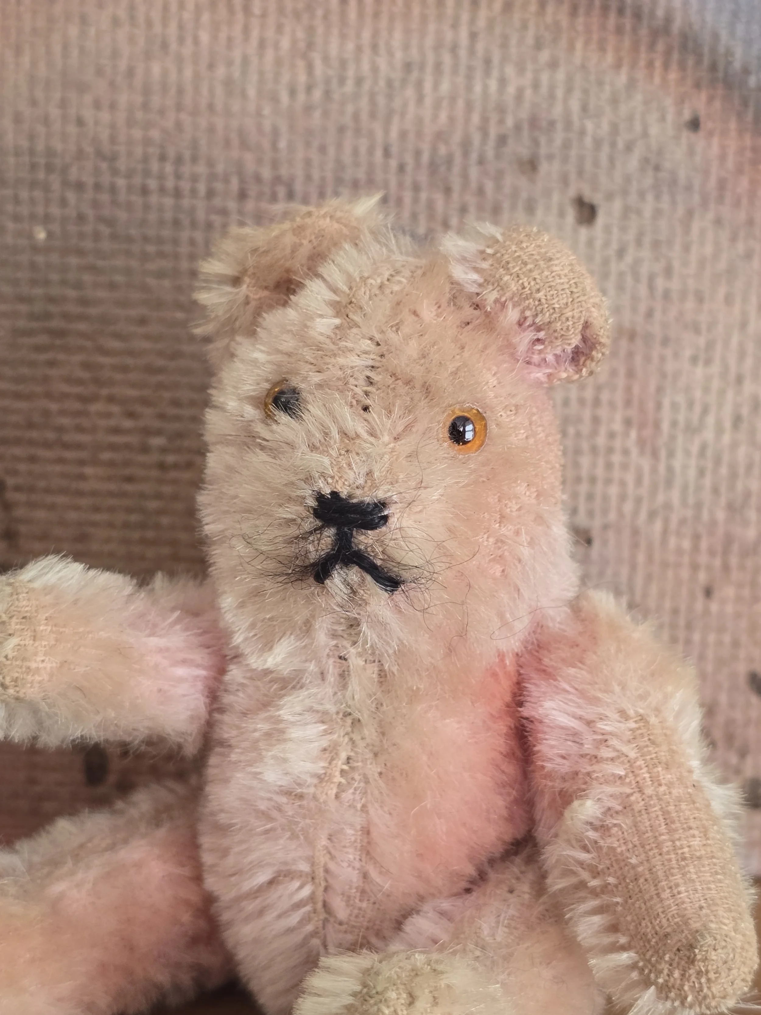 Close-up of a miniature pink teddy bear showing stitched features and age-related wear.