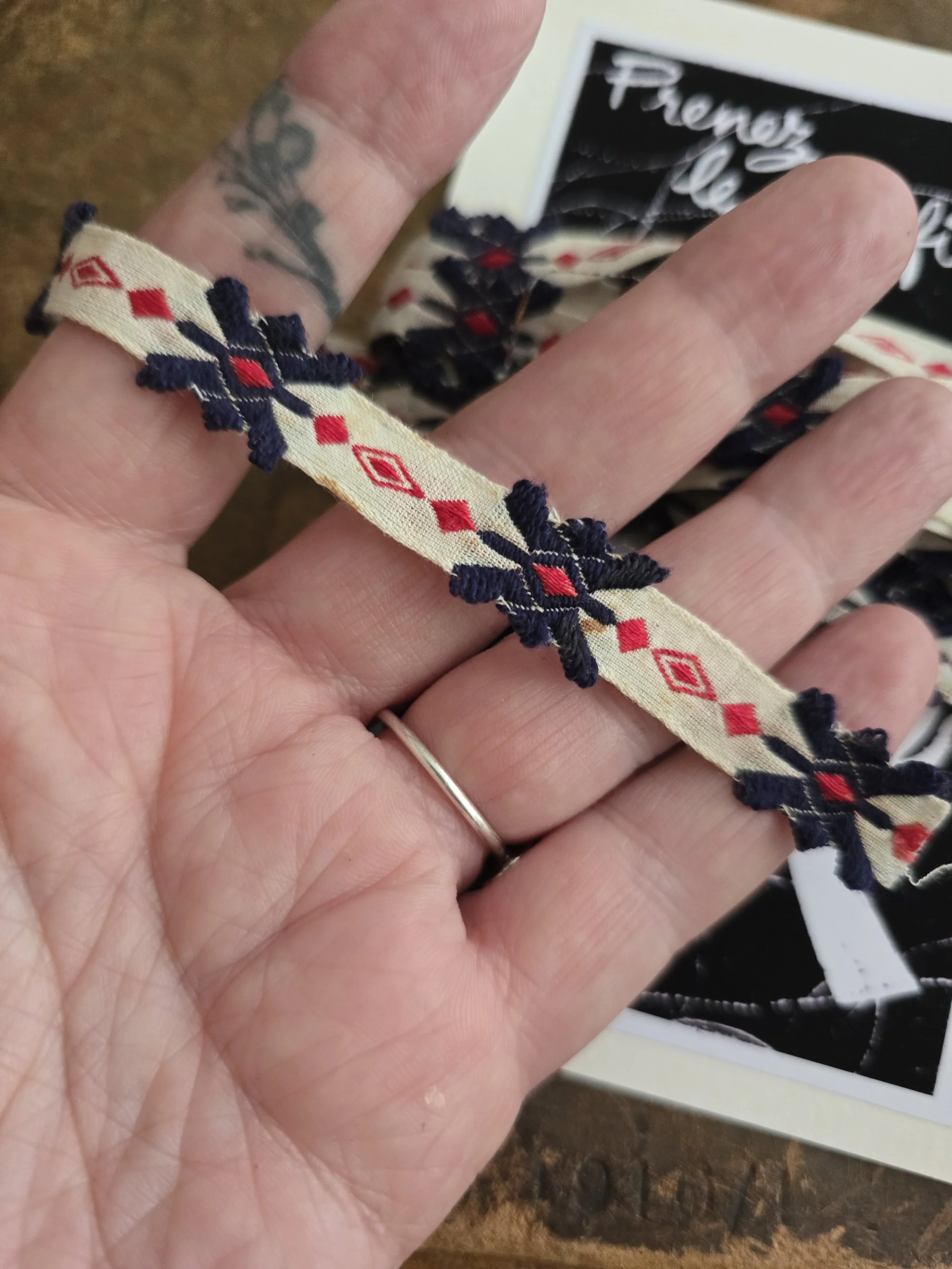 Vintage French textile trim shown across a hand for scale, measuring 0.5 cm wide with navy and red woven details.