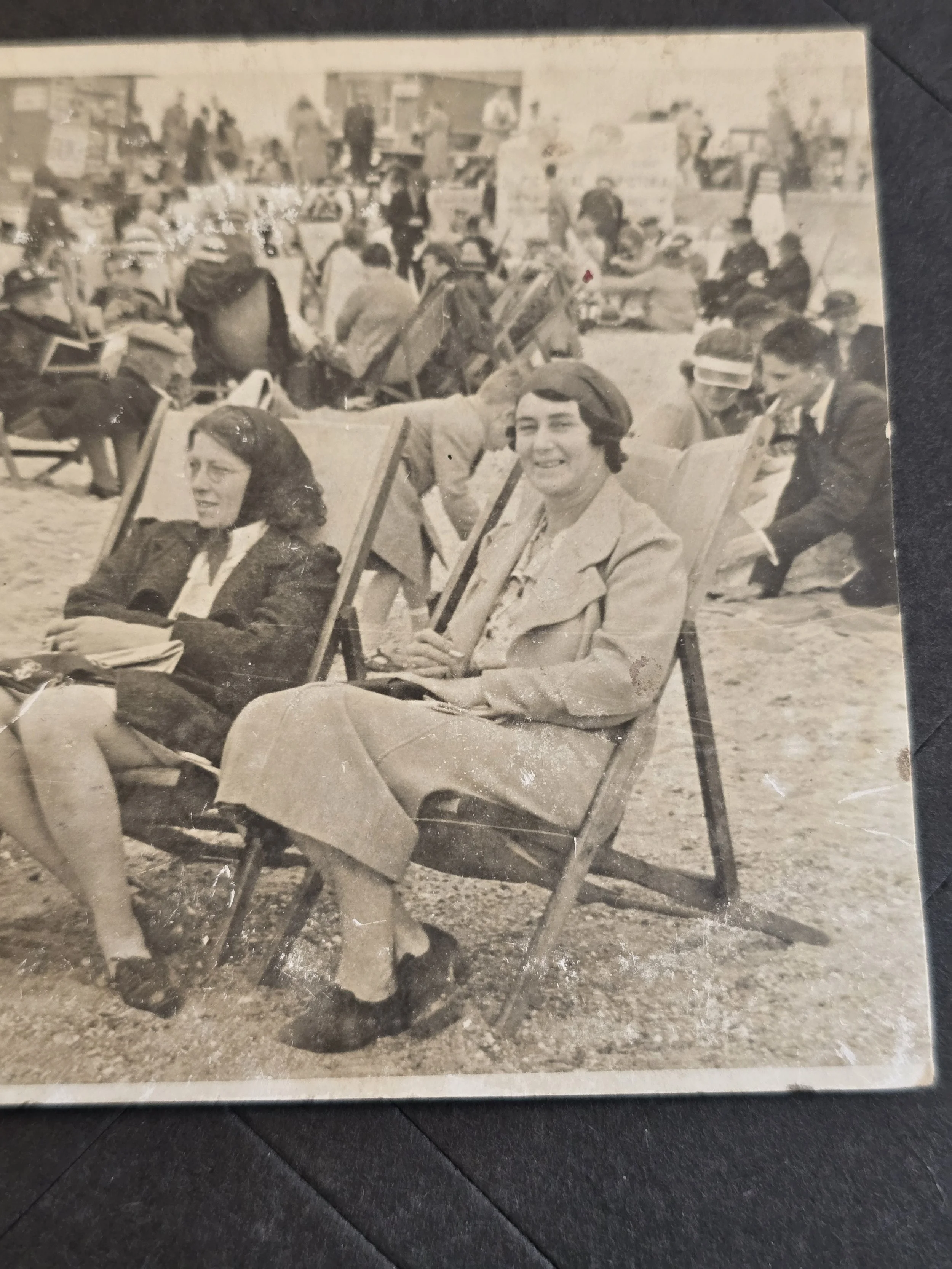 Close-up of three women relaxing in traditional canvas deckchairs in a vintage seaside photograph.