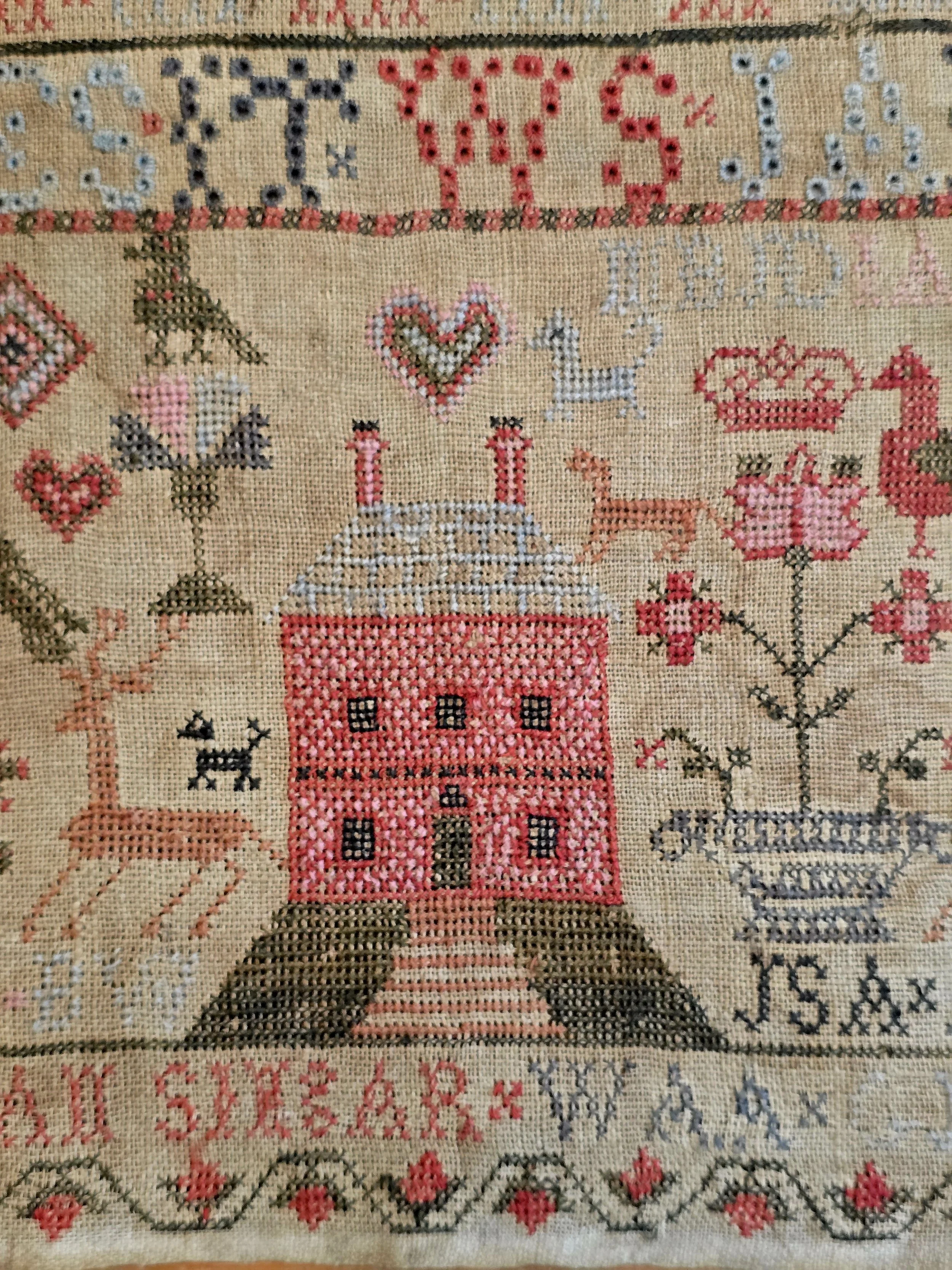 Close-up of the central pink house and floral motifs on an 18th century Scottish embroidered sampler.