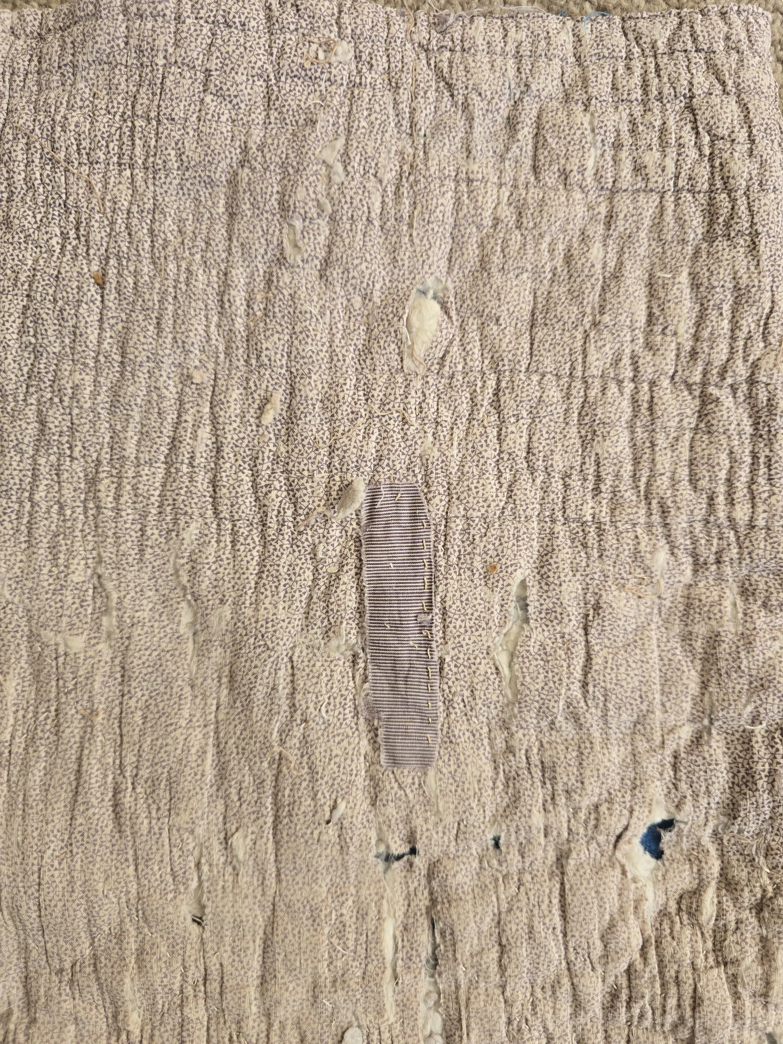 Antique French quilt fragment with faded purple printed cotton and exposed layers.