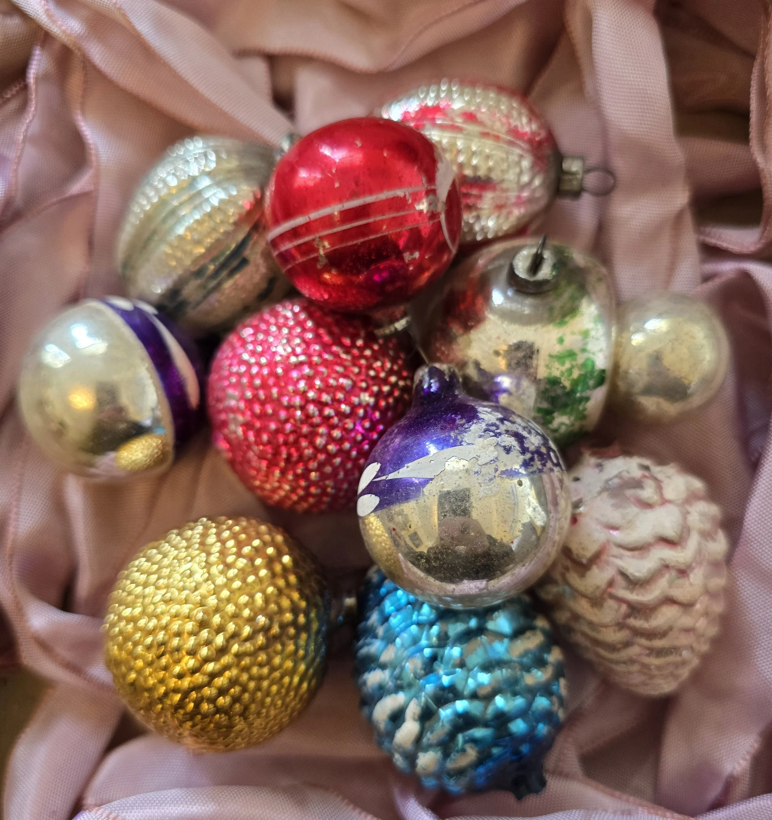Close-up of vintage glass Christmas baubles with textured silver surfaces and faded red and blue painted stripes.