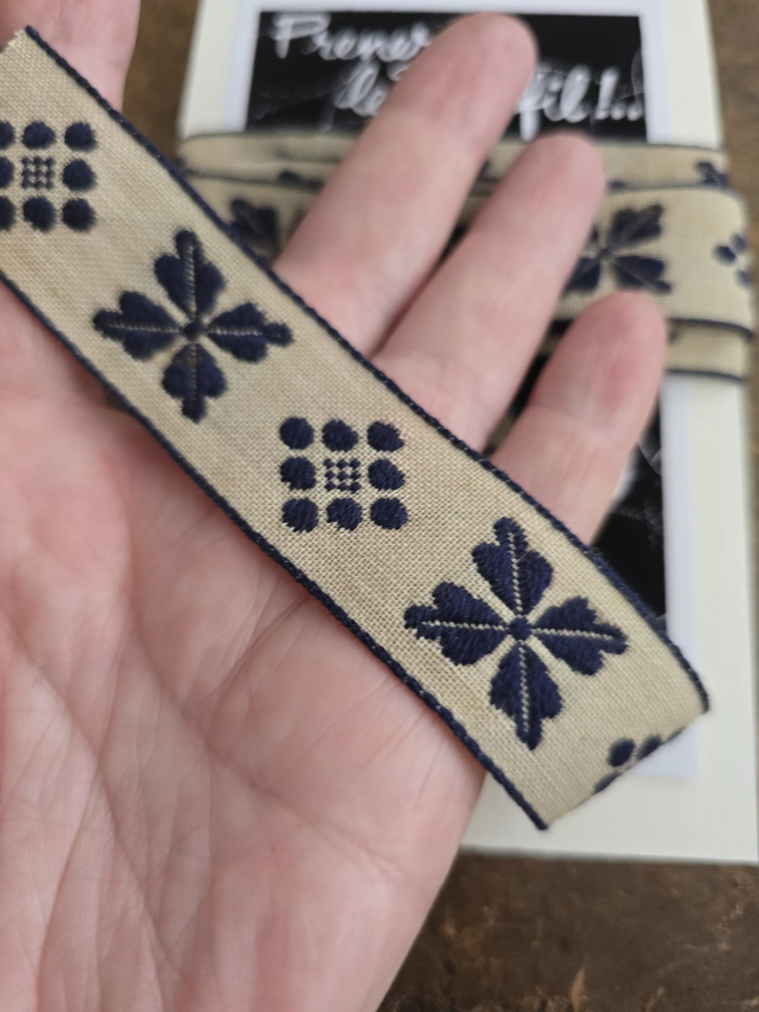 Detail of cream and navy vintage trim held by hand showing the scale and woven design.