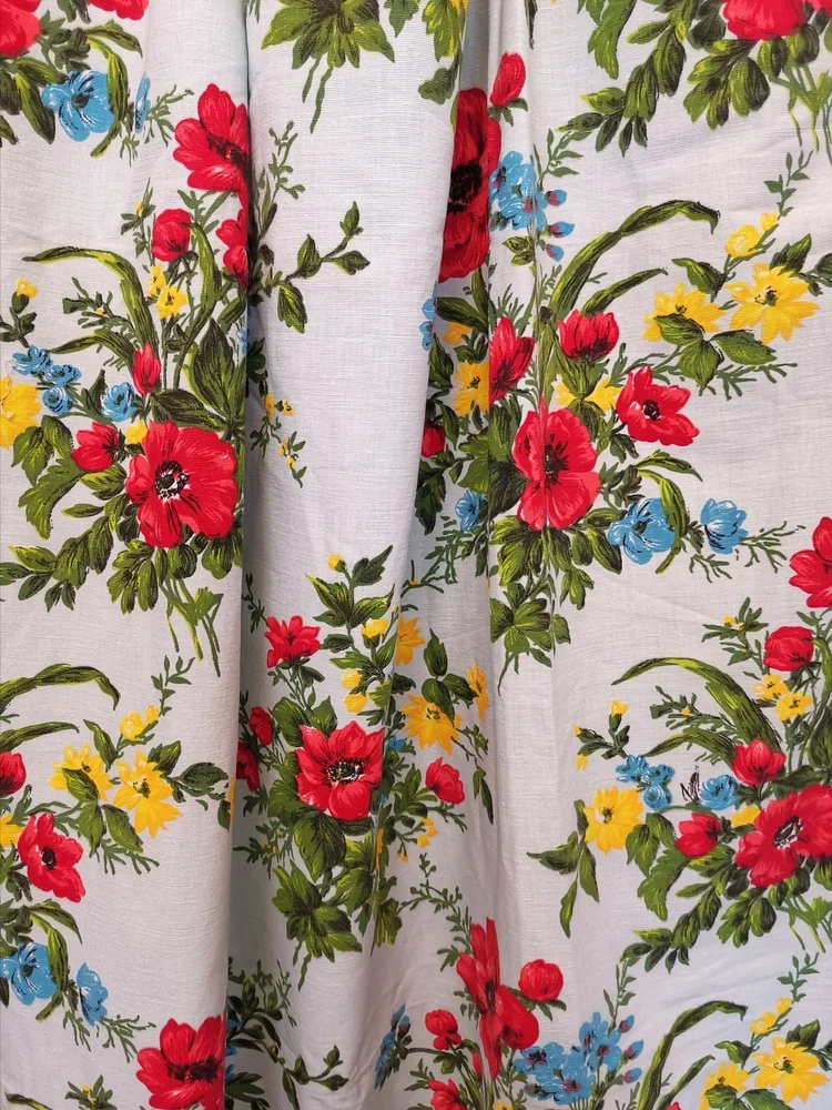 Horizontal view of large red poppy with green foliage on vintage floral cotton fabric.