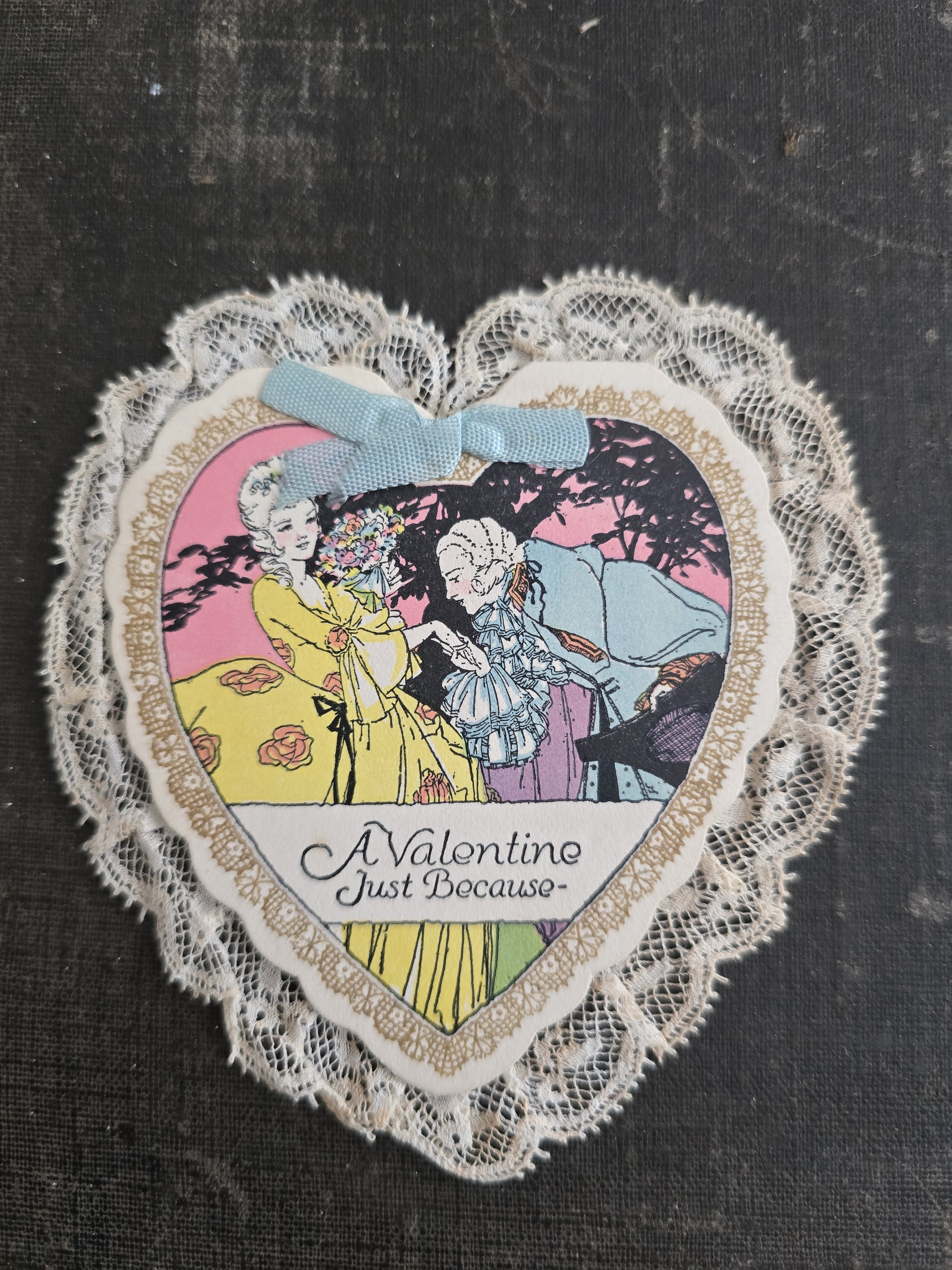 Vintage heart-shaped Valentine card with cream lace edging, blue ribbon and colourful romantic illustration.