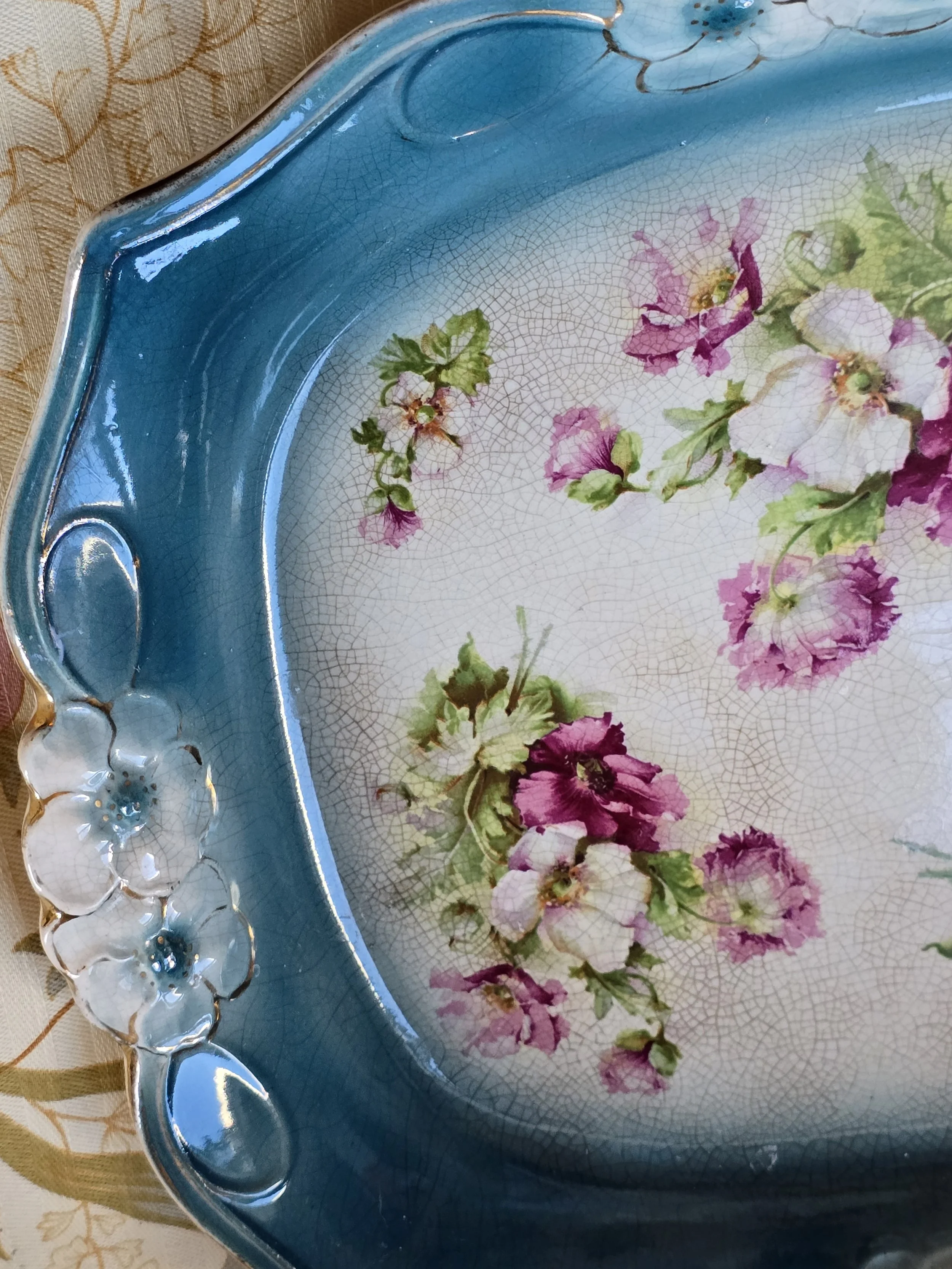 Close-up of crazed vintage ceramic tray with pink floral sprays and raised white flowers with gilt details.