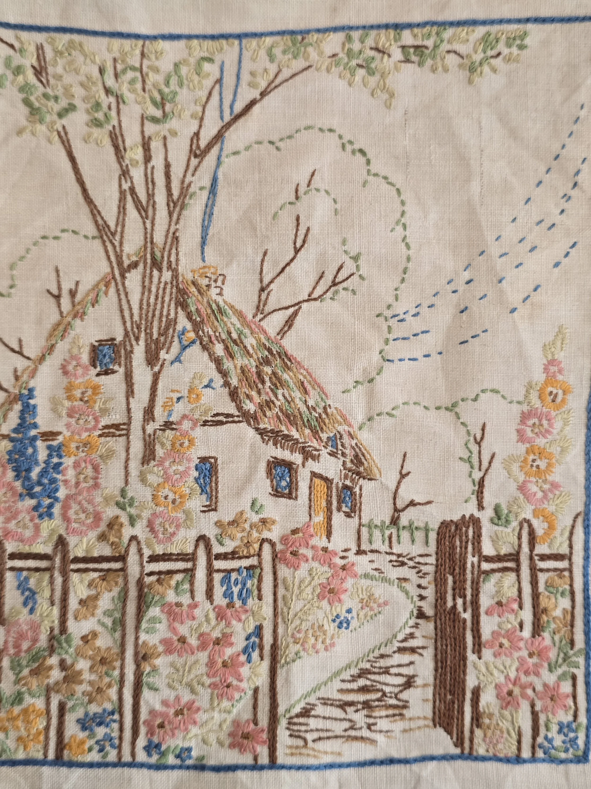 Hand stitched vintage embroidery showing a cottage surrounded by colourful flowers.