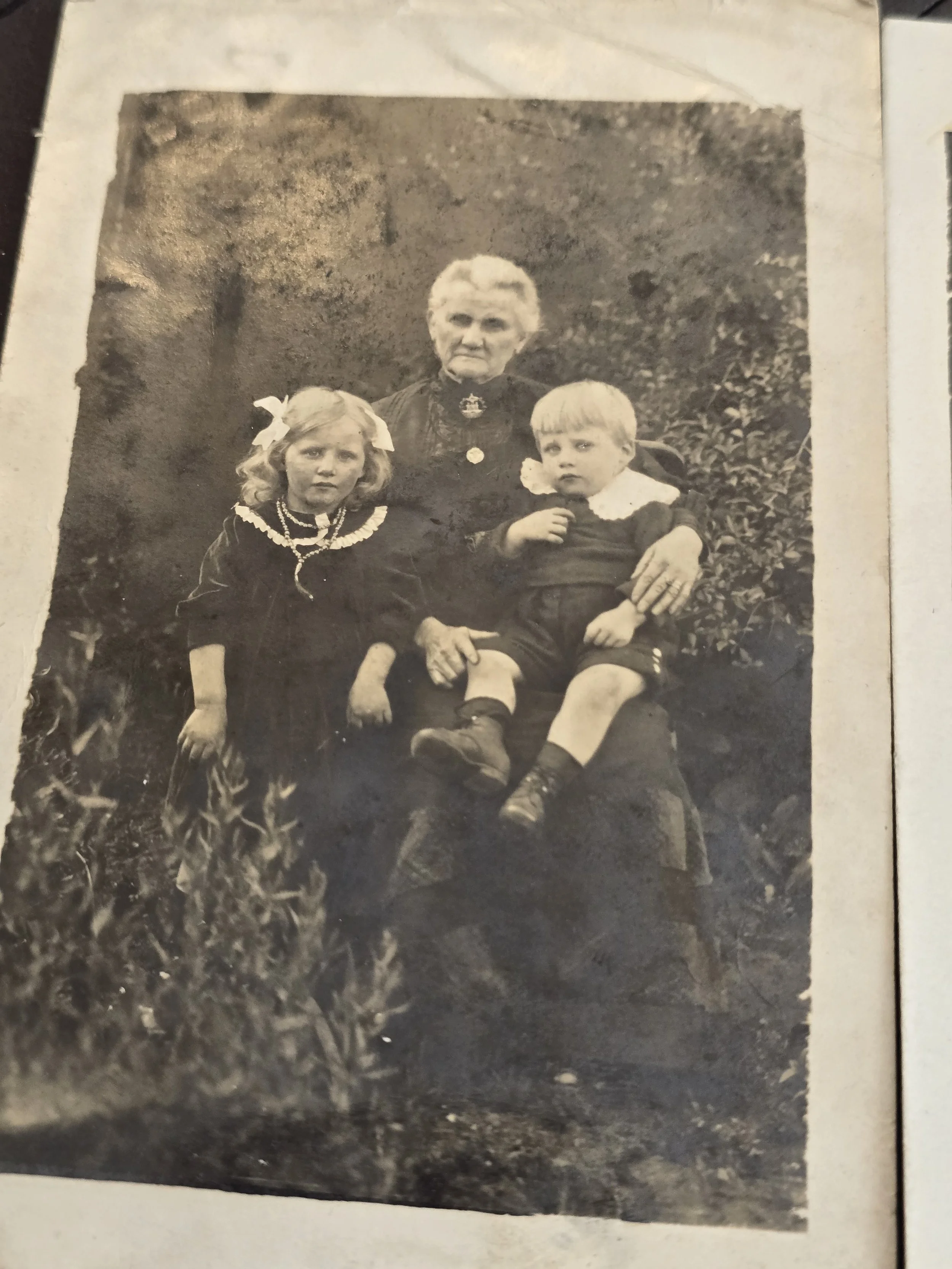 Antique photograph of an elderly woman seated with a young girl and small boy, c.1910–1920.