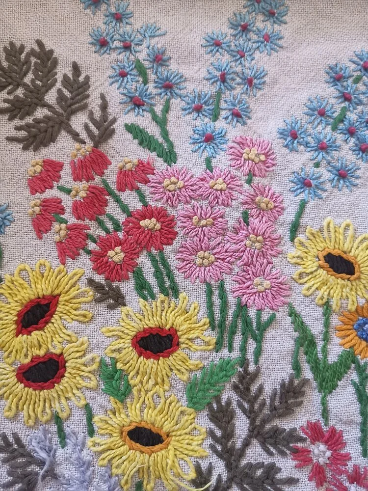 Close-up of densely stitched floral corner in red and orange on rustic hemp fabric