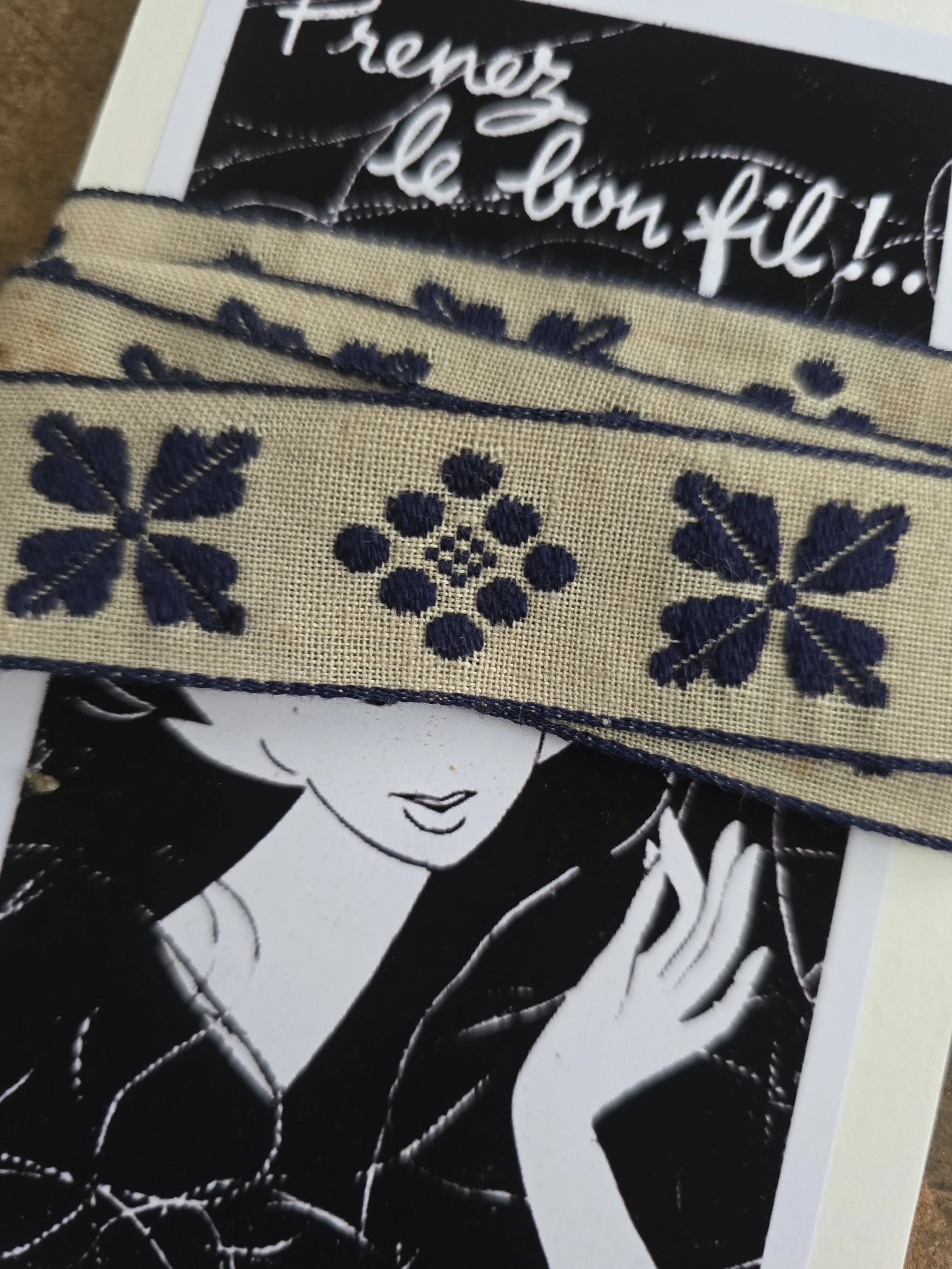 Close-up of vintage woven textile braid showing deep blue embroidered flower and leaf motifs.