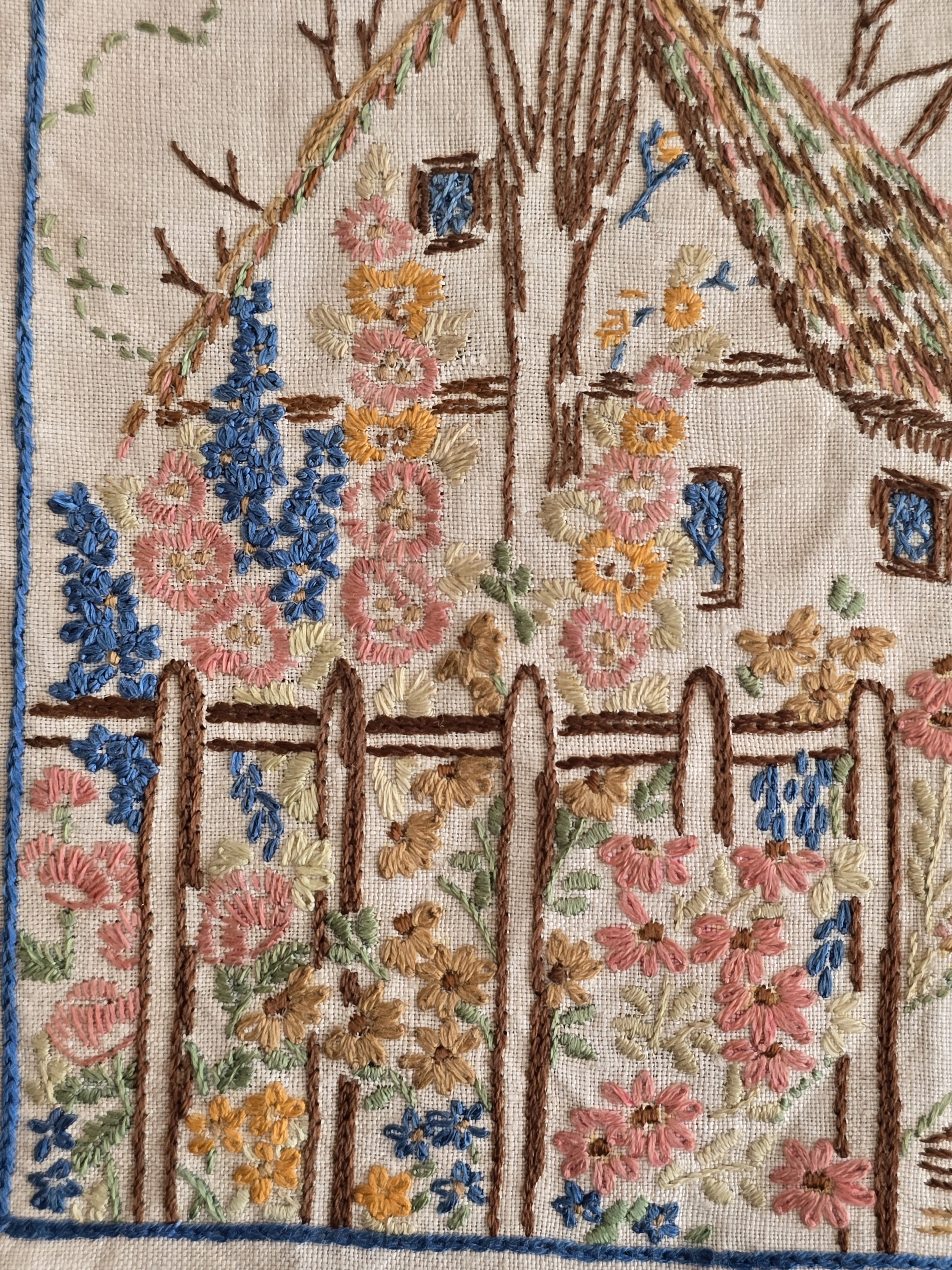 Detail of vintage cottage garden embroidery with pink and blue blooms.