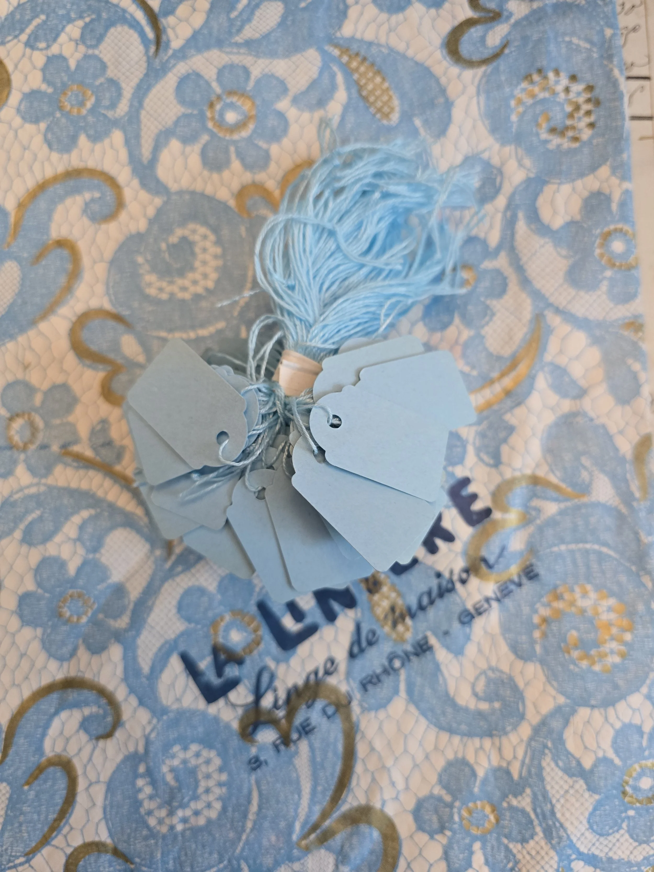 Bundle of 100 vintage French pale blue paper price tags with original blue threads, photographed on vintage French packaging.