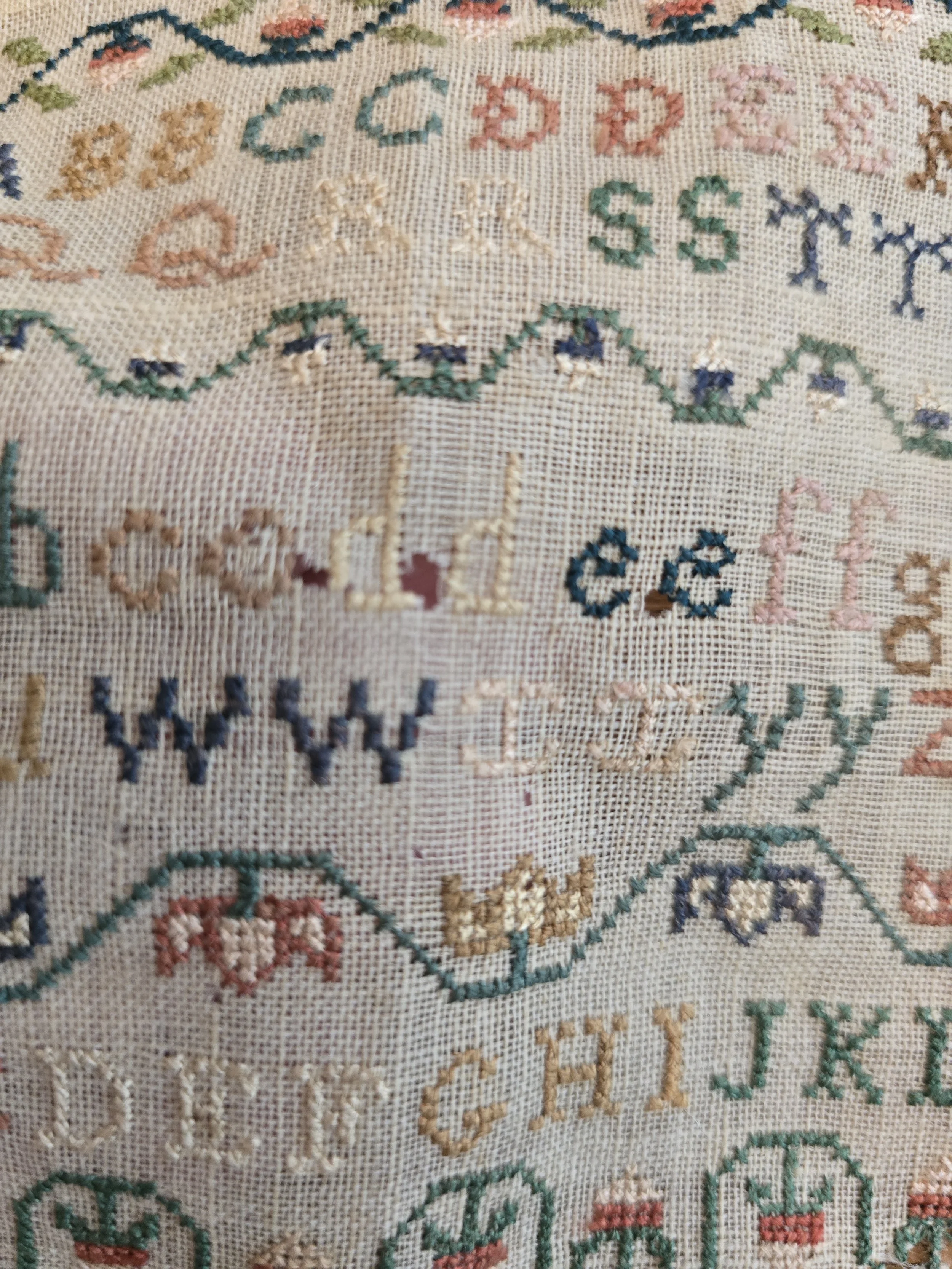Antique educational sampler displaying upper and lower case letters, numbers and decorative borders.