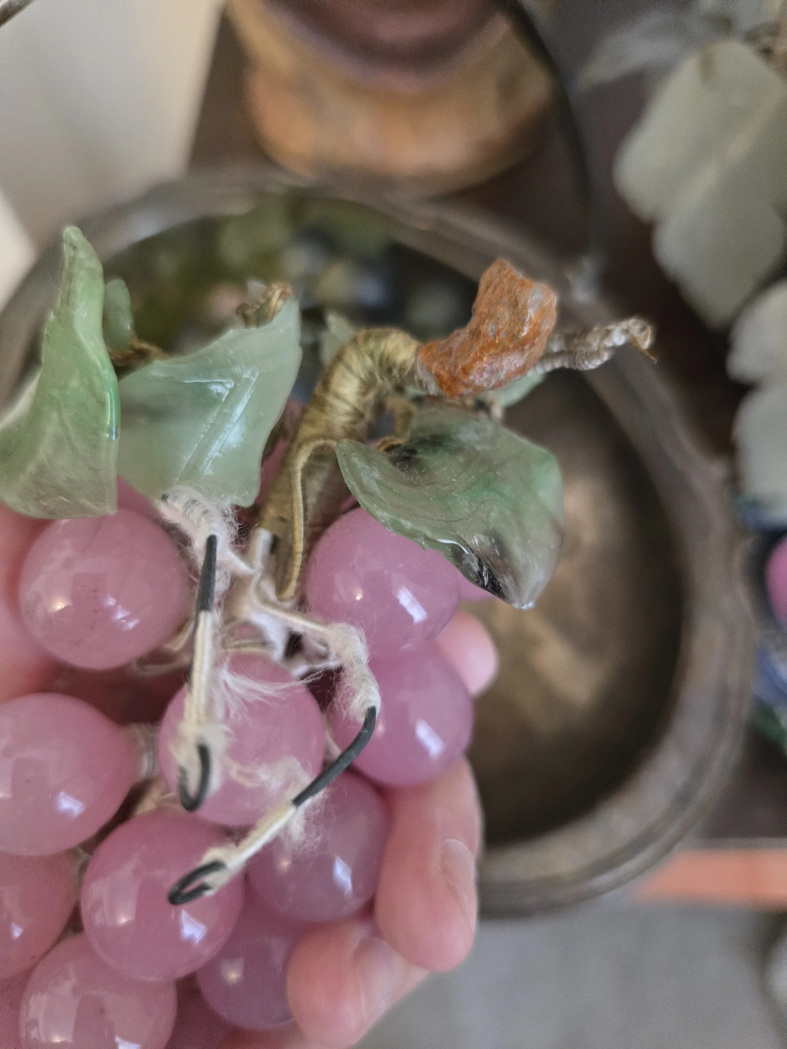 Close-up of the top of vintage glass grape cluster showing green glass leaves, wrapped stems and age-related damage.