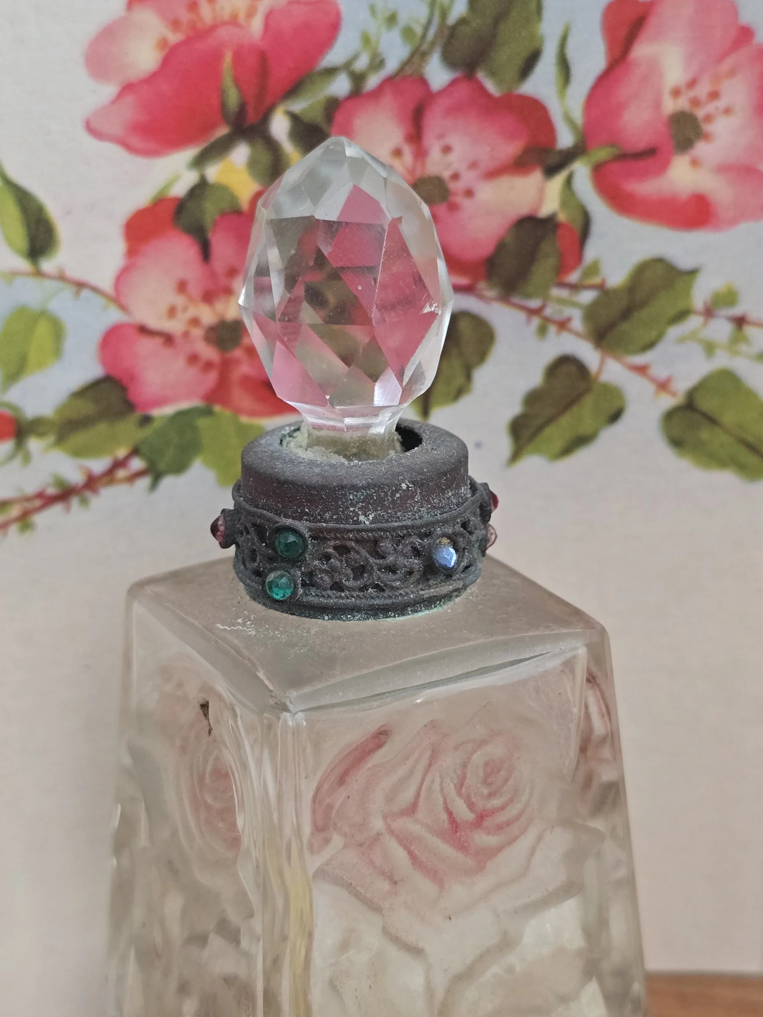 Close view of the faceted glass stopper and ornate jewelled metal collar on an antique perfume bottle.