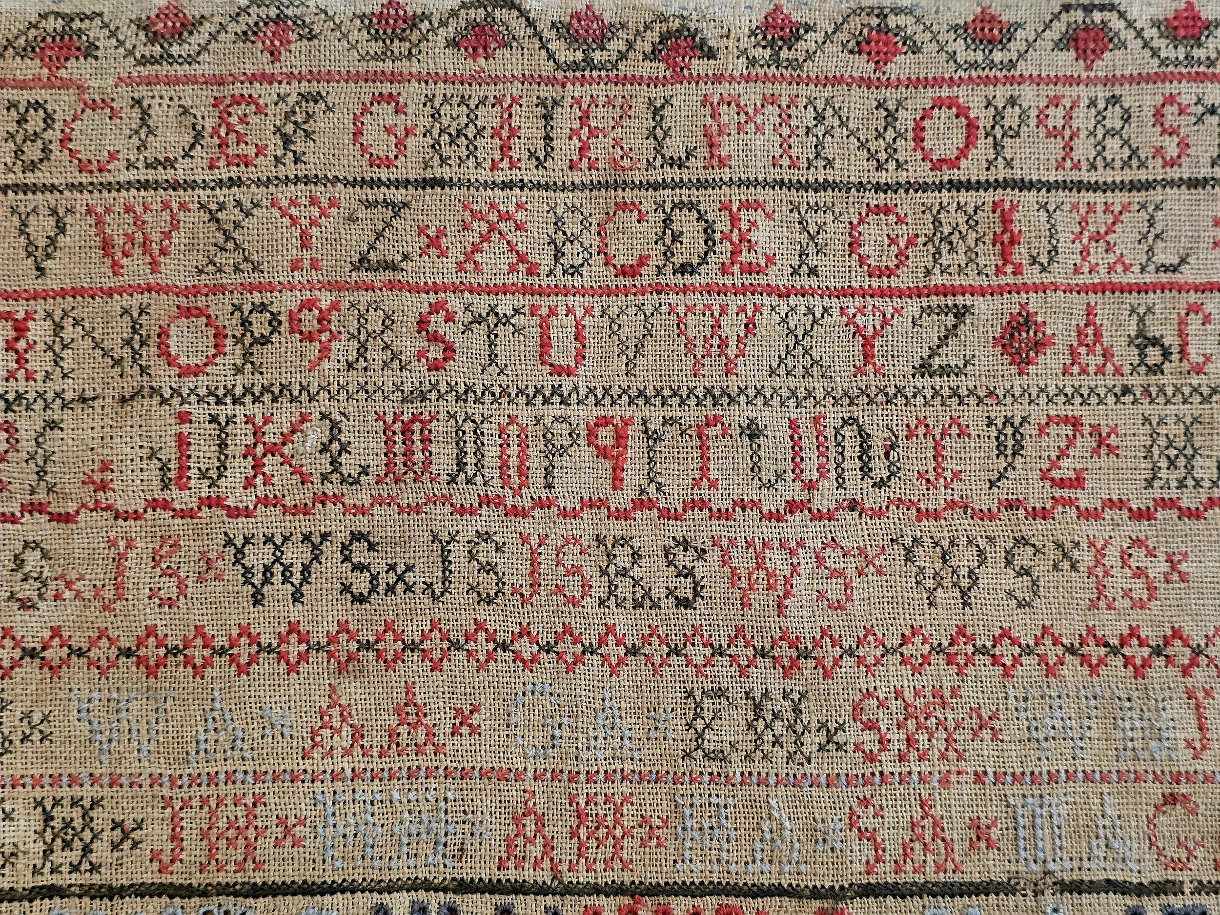 Detail of the embroidered birds, crowns and alphabet rows stitched in faded silk on Georgian linen.