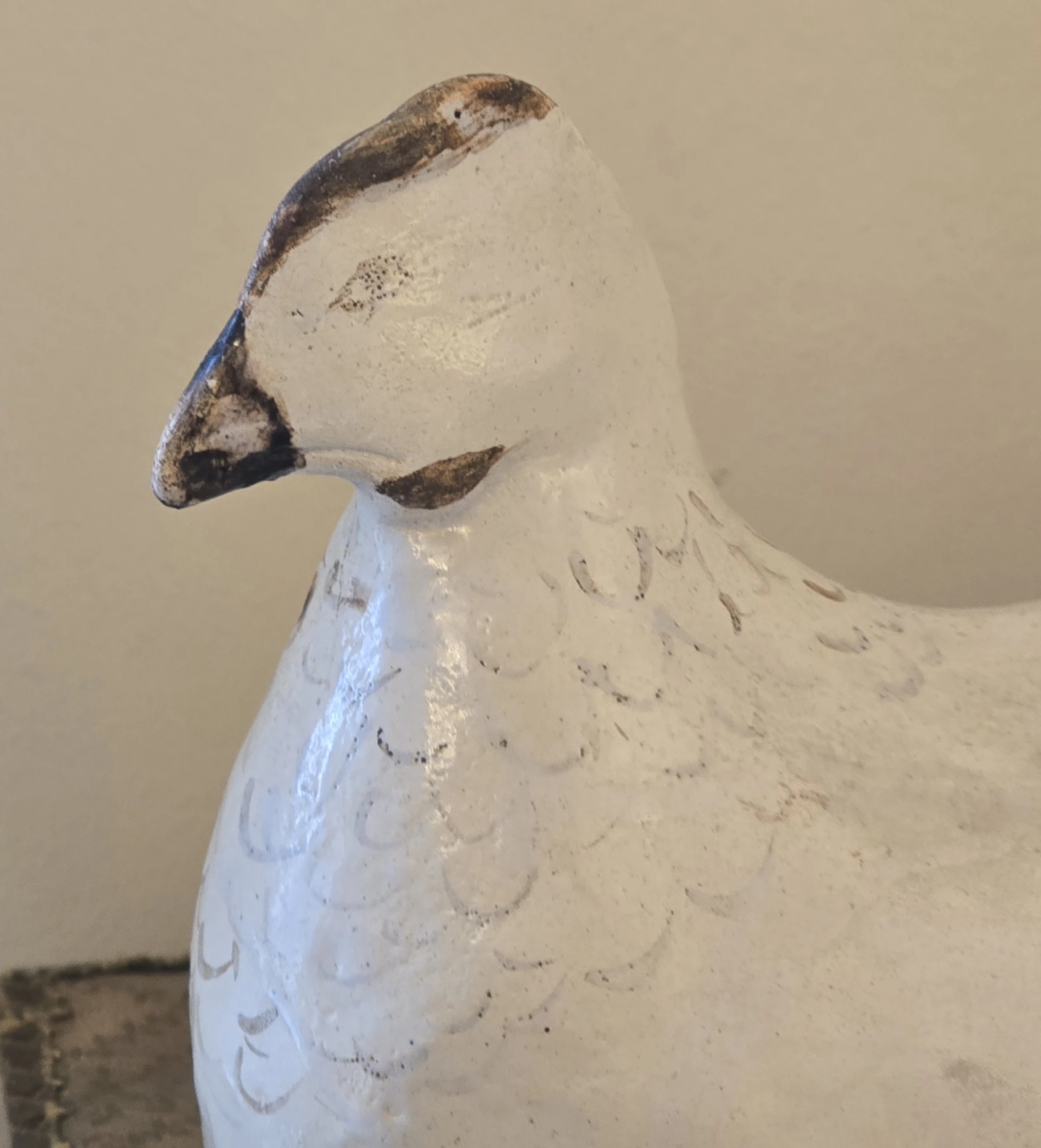 Close-up of the hen's head with worn dark painted beak and softly faded feather markings.