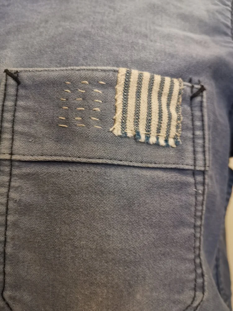 Chest Pocket Detail – Mended pocket with visible sashiko running stitches and patchwork edge.