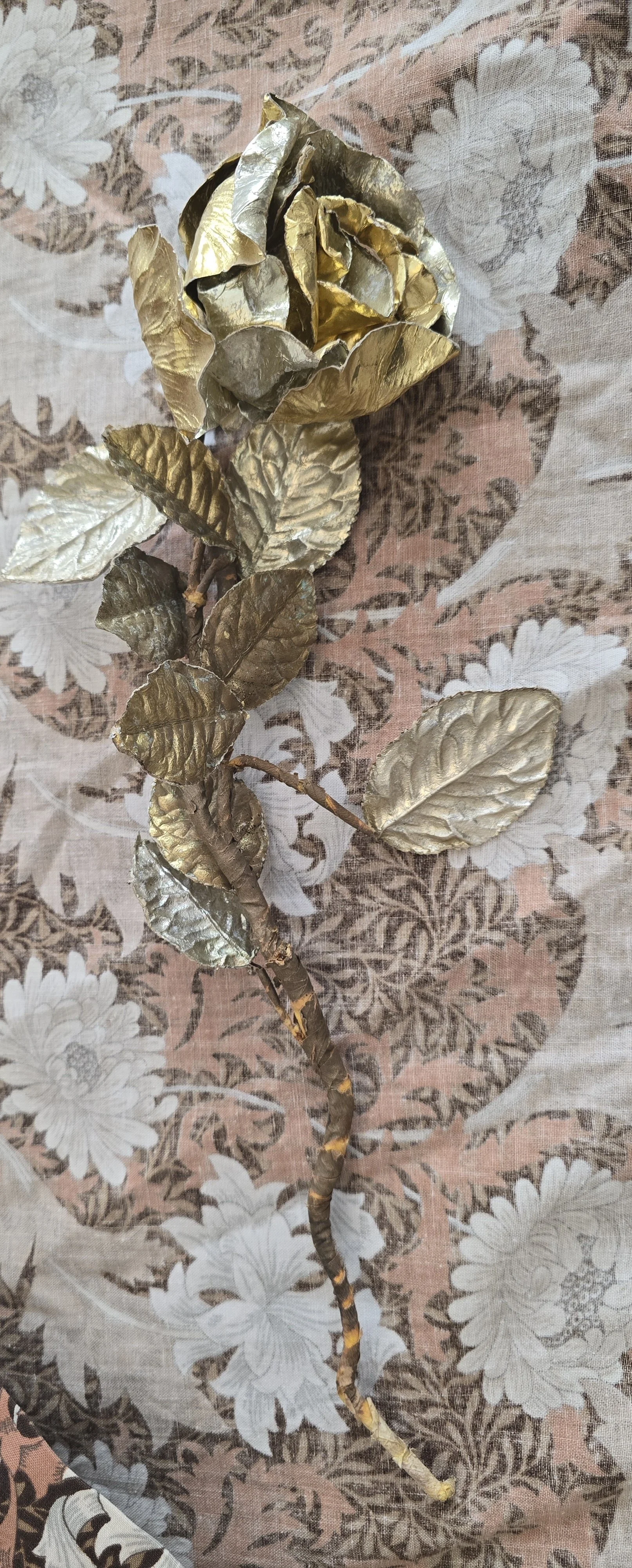 Vintage decorative gold rose stem with embossed metallic leaves and aged patina.