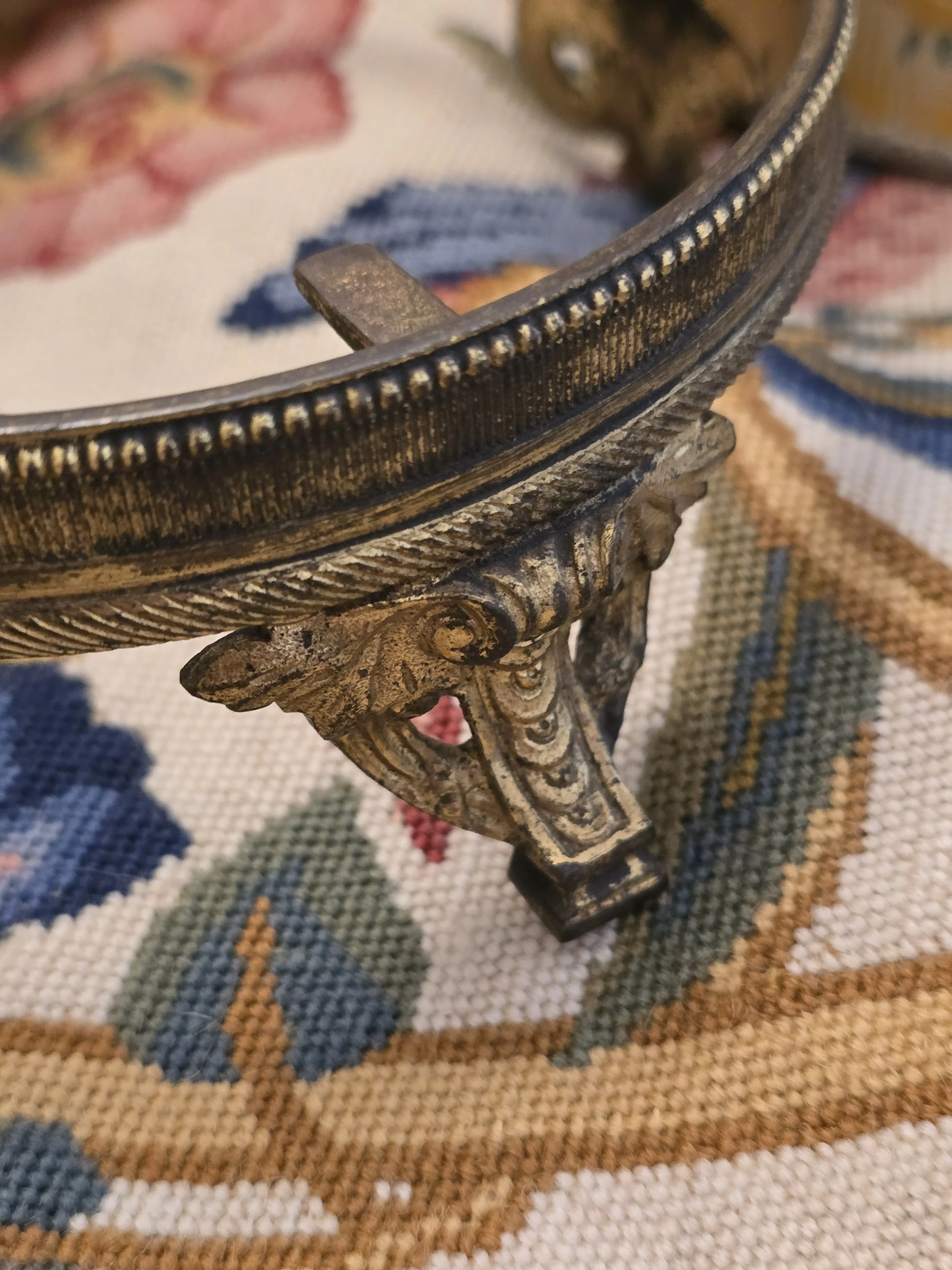 Close-up of decorative metal stand showing beaded edging and an ornate scrolling foot.