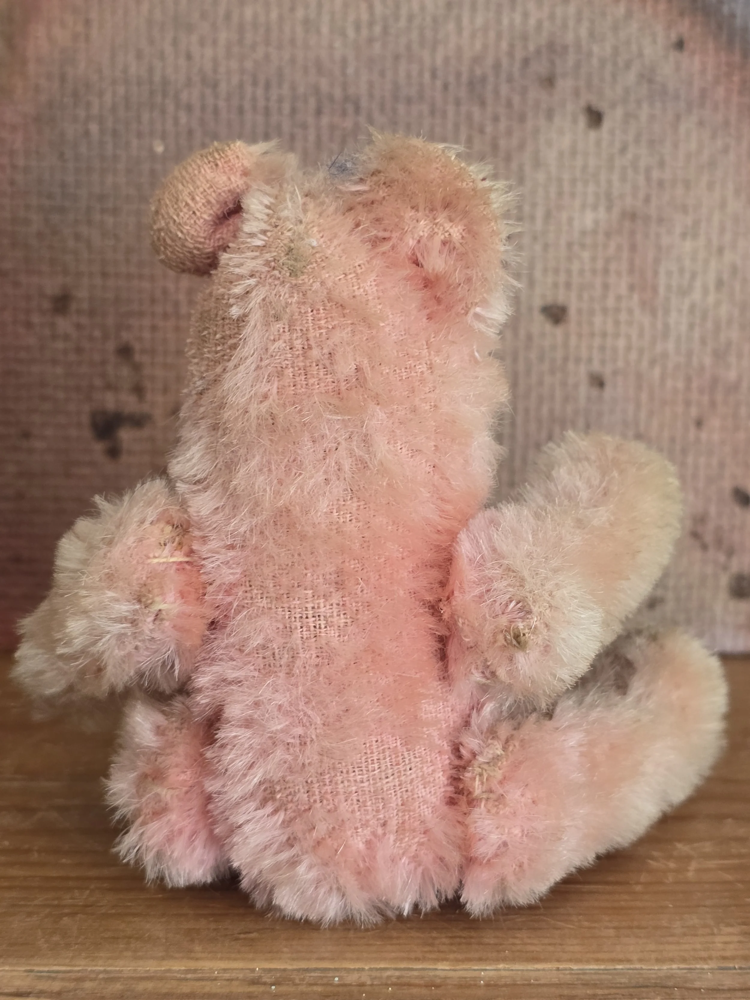 Back view of a small vintage pink teddy bear with faded plush covering.